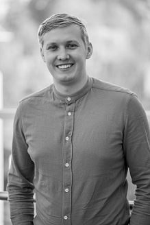 Smiling person in a buttoned shirt standing outdoors, shown in black and white