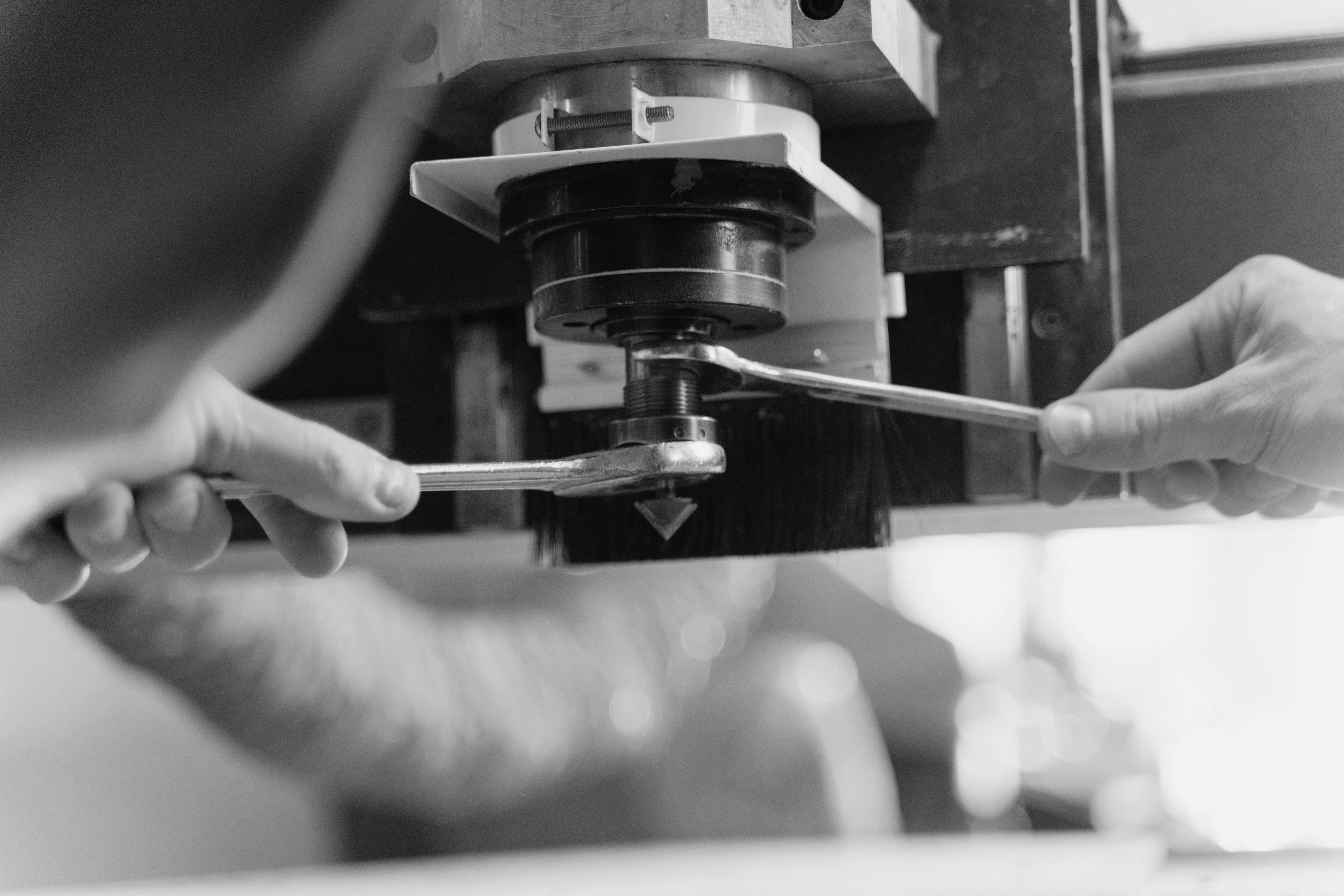 Two people use wrenches to adjust a spindle on an industrial machine.