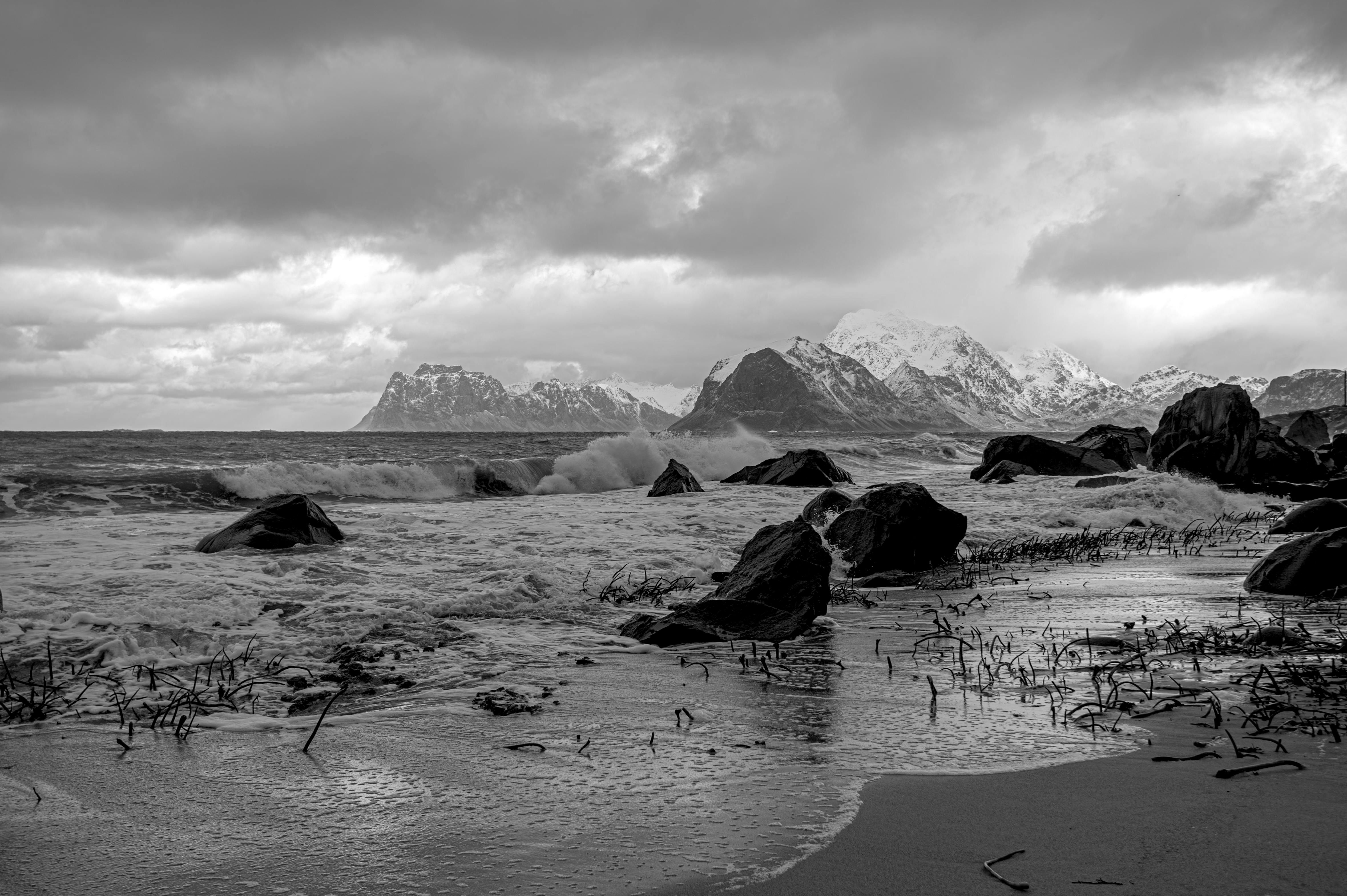 Stormy waves crash on a rocky shore with snow-covered mountains in the distance