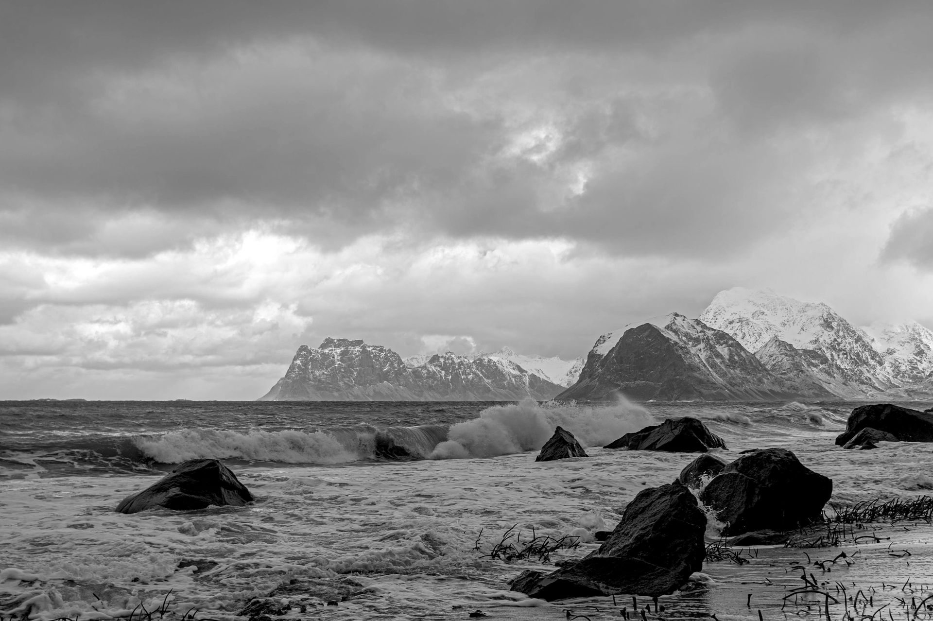 Stormy waves crash on a rocky shore with snow-covered mountains in the distance