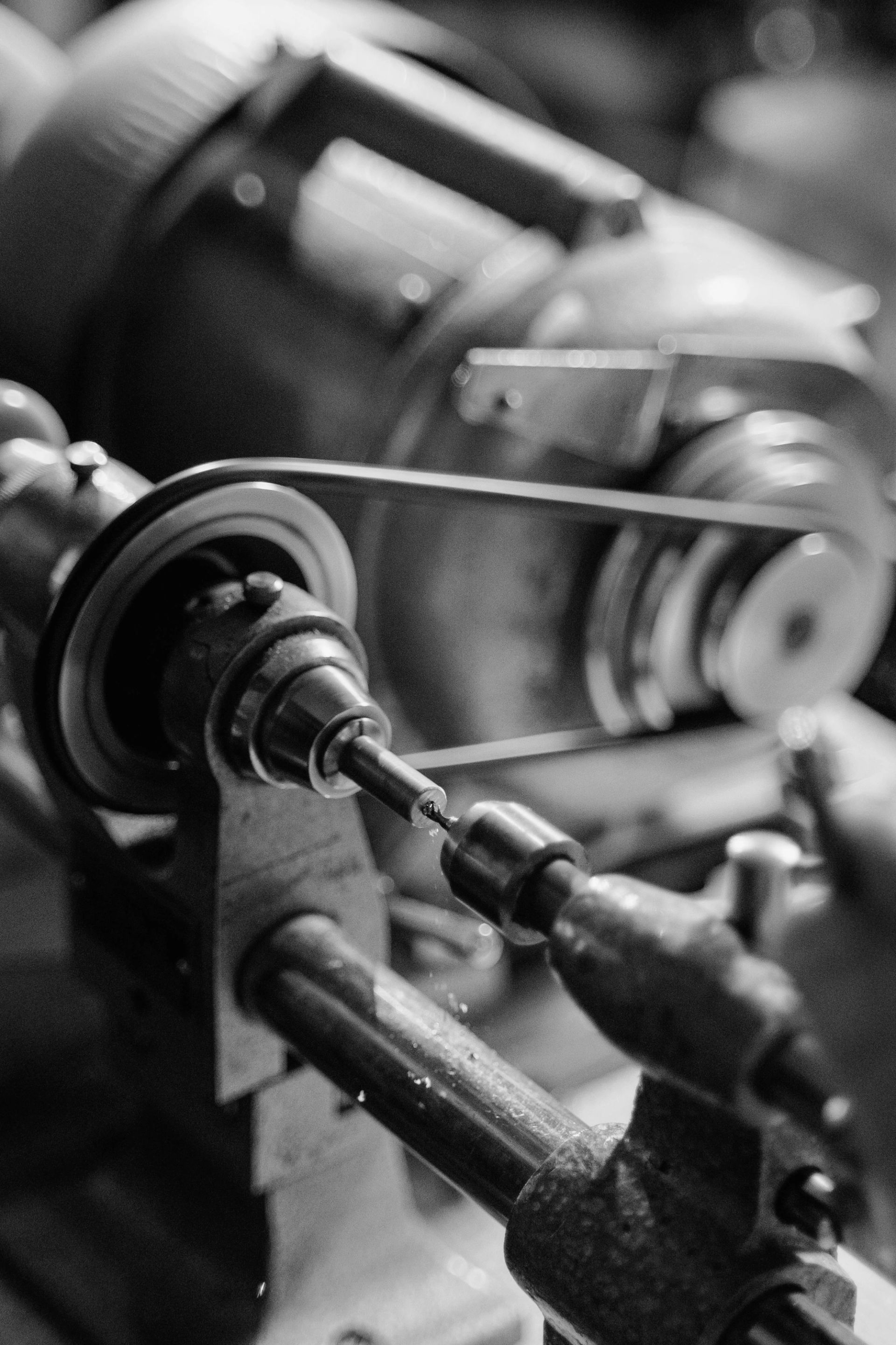 Black-and-white close-up of a belt-driven metal lathe drilling a small workpiece