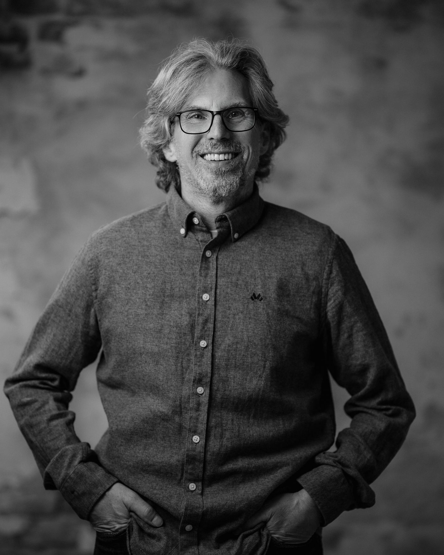 Smiling middle-aged person with glasses and beard in a black-and-white portrait
