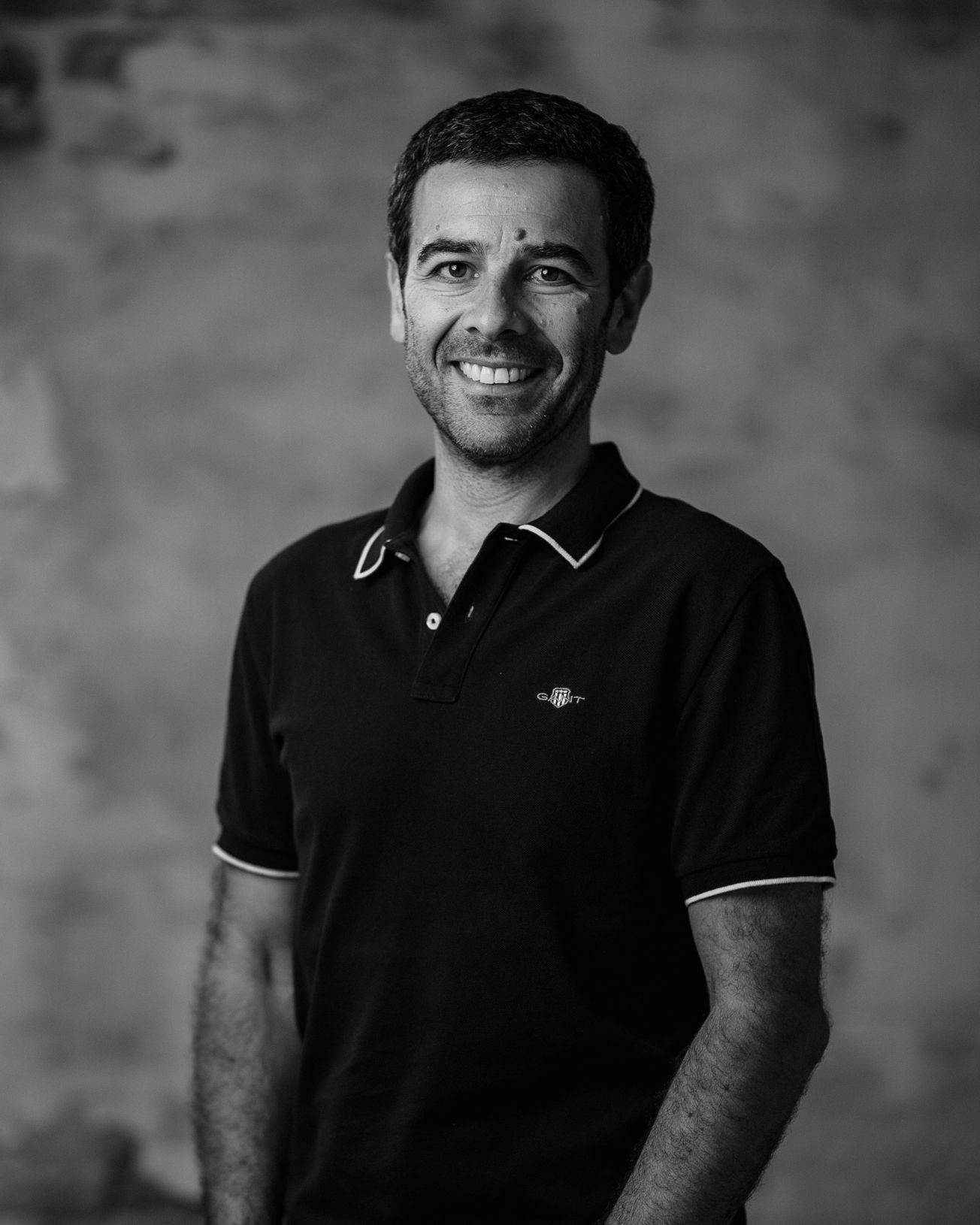 Smiling man in a dark polo shirt standing against a plain blurred background