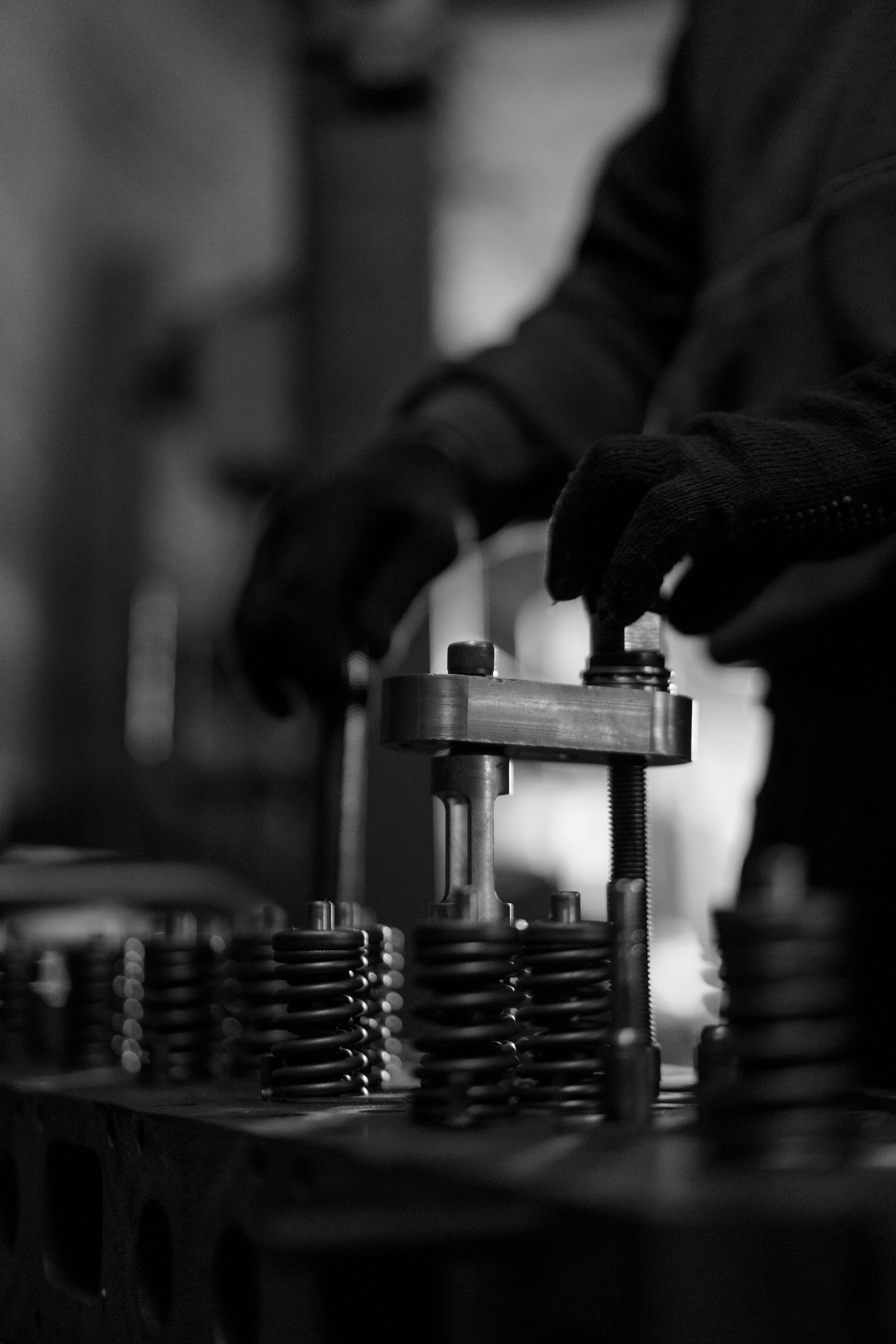 Gloved hands operate a metal press above rows of coiled springs in a workshop.