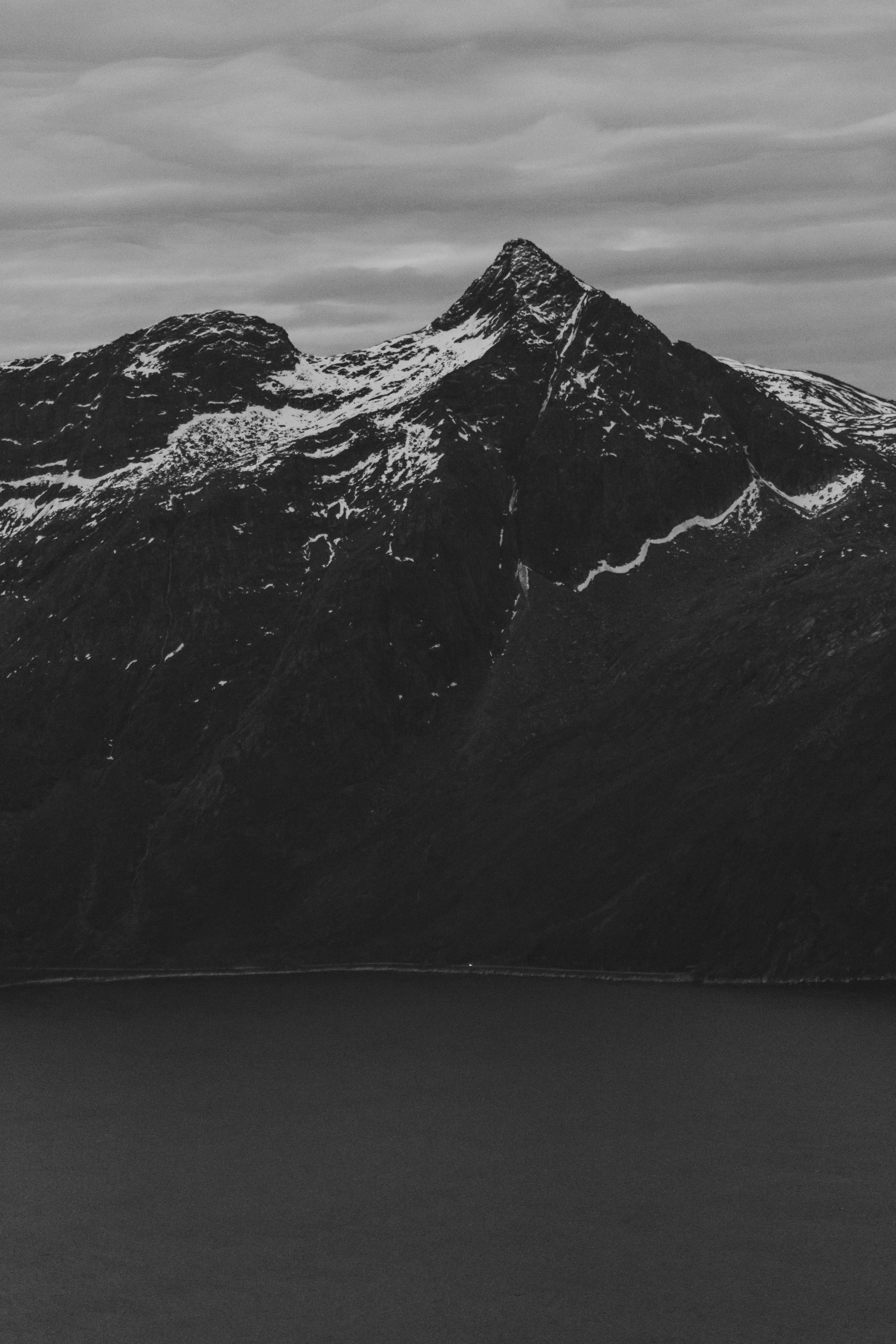 Black-and-white view of a snow-streaked mountain rising above calm water