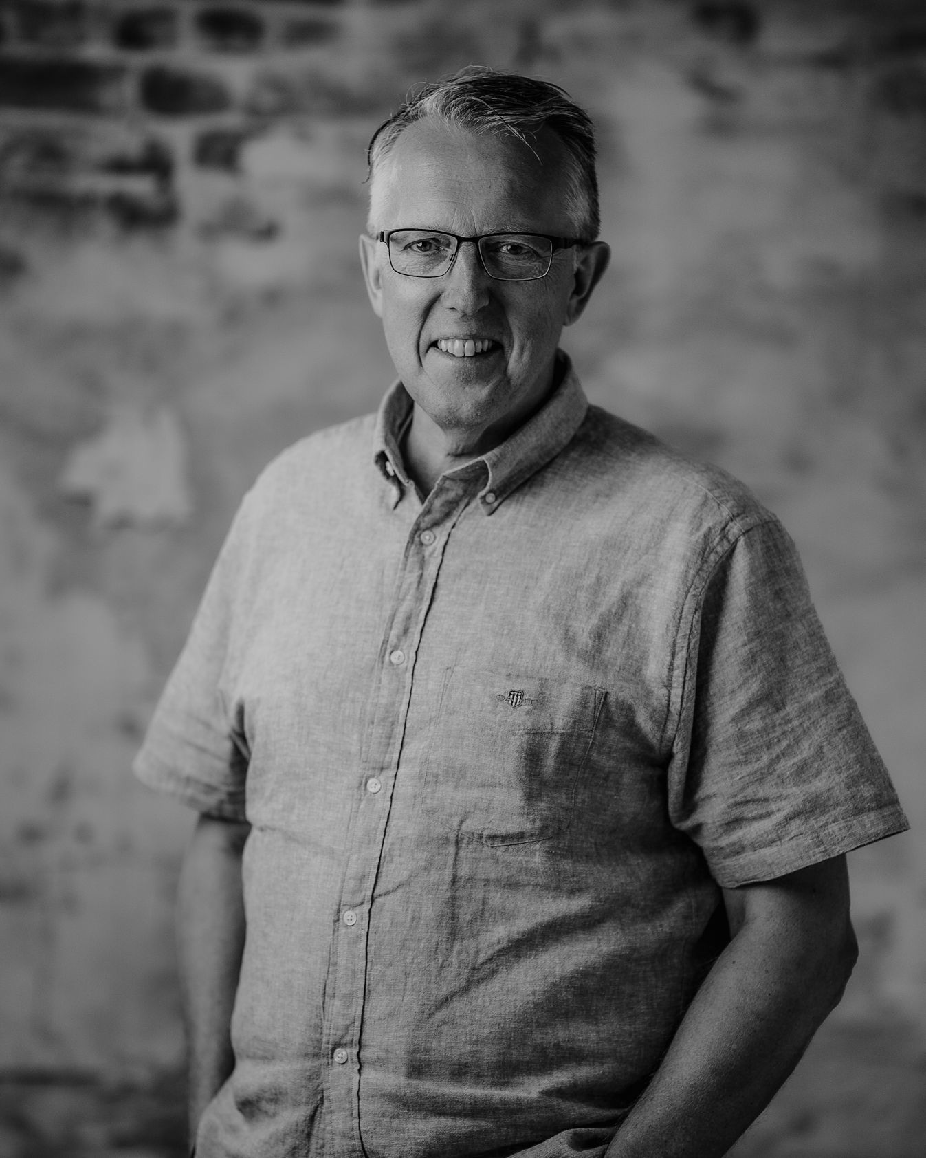 Black-and-white close-up of a middle-aged man wearing glasses, looking at the camera