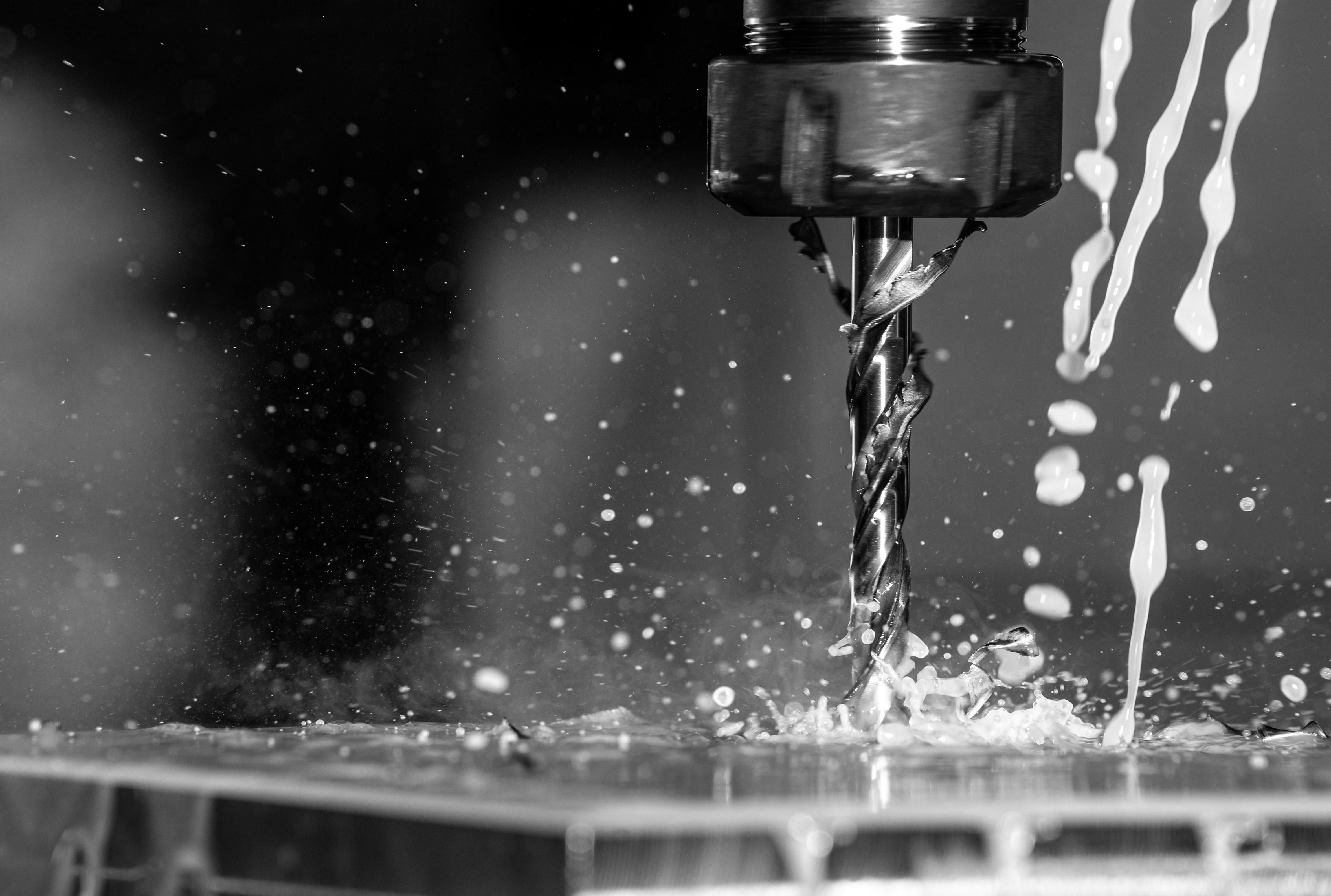Close-up of a drill bit cutting metal with coolant and sparks spraying around