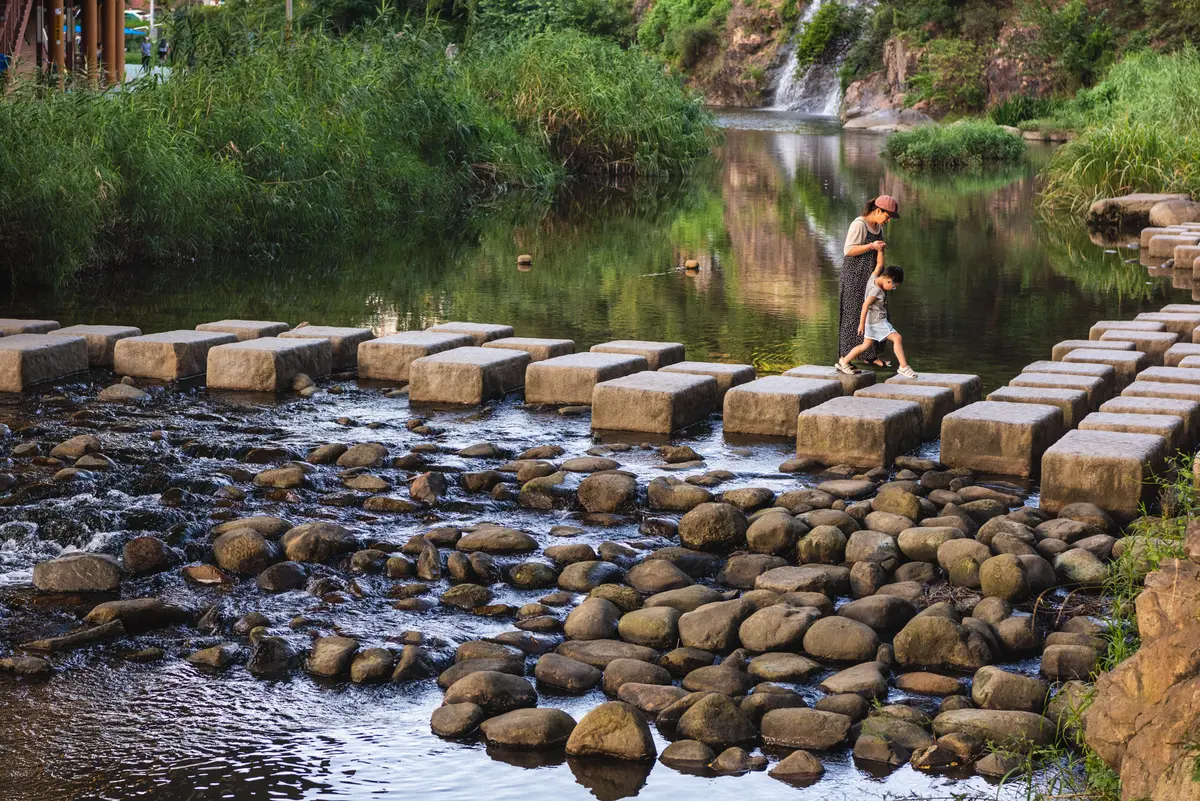 Korean mother helps her son cross a river path by a waterfall at the Hongjecheon stream in Seoul