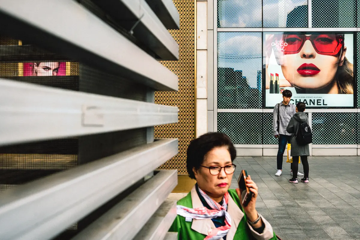 A middle-aged woman passes by a couple having an argument in front of a building with luxury goods advertisements on the wall in Yeongdeungpo-gu, Seoul