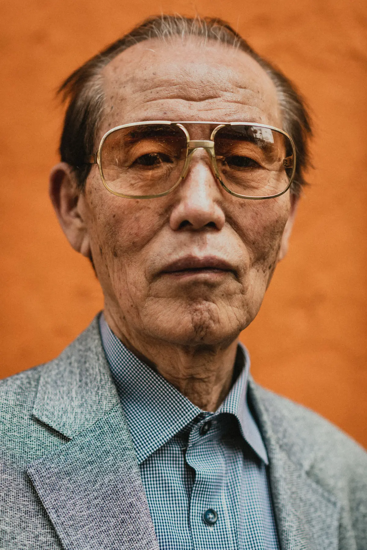 Close-up portrait of an elderly Korean man wearing orange-tinted glasses