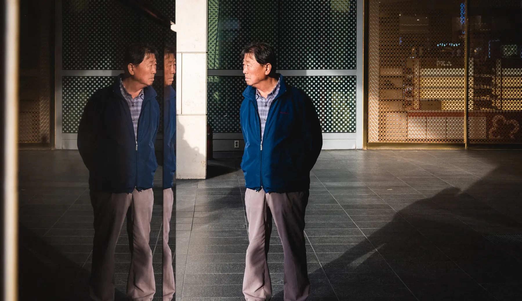 Korean man's image is reflected in a mirror as he stands in strong sunlight in Yeongdeungpo-gu, Seoul