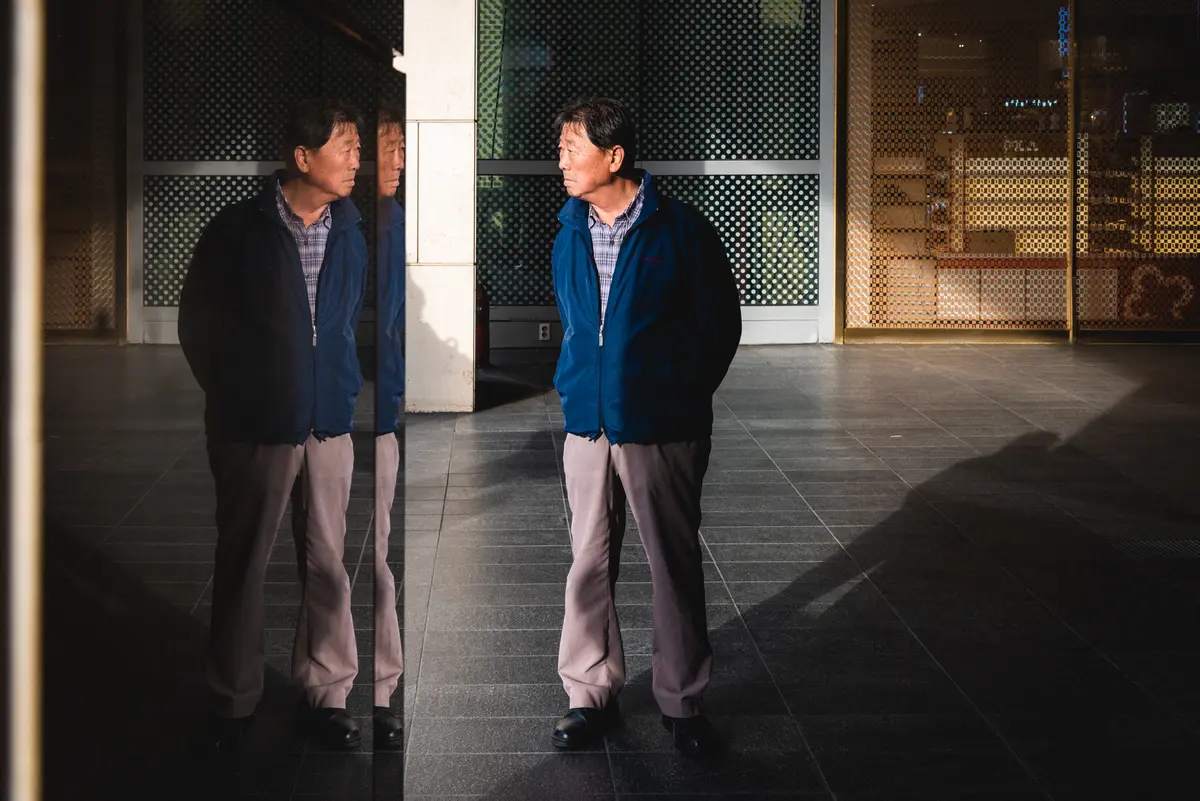 Korean man's image is reflected in a mirror as he stands in strong sunlight in Yeongdeungpo-gu, Seoul