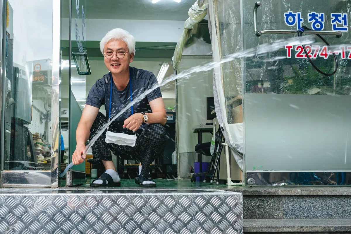 Korean man with white hair sprays water out of a hose while squatting at a storefront in Euljiro, Seoul