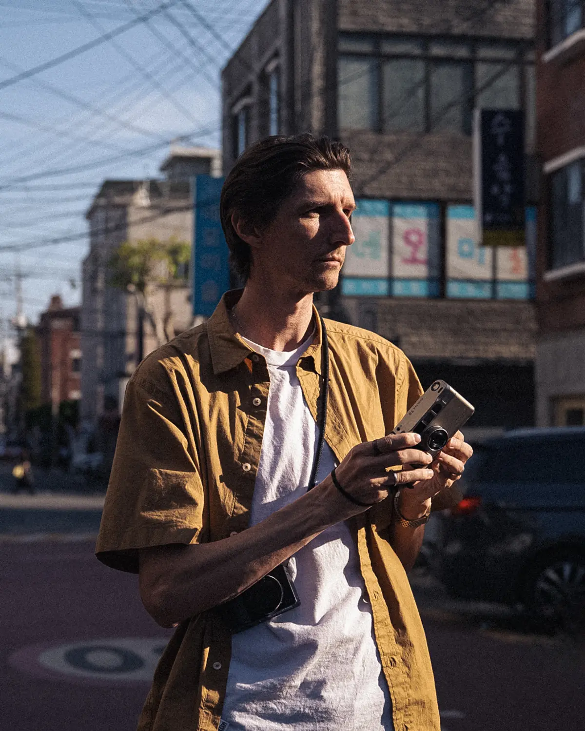 Portrait photo of Chris standing in a patch of afternoon sunlight, boasting a pair of sunglasses