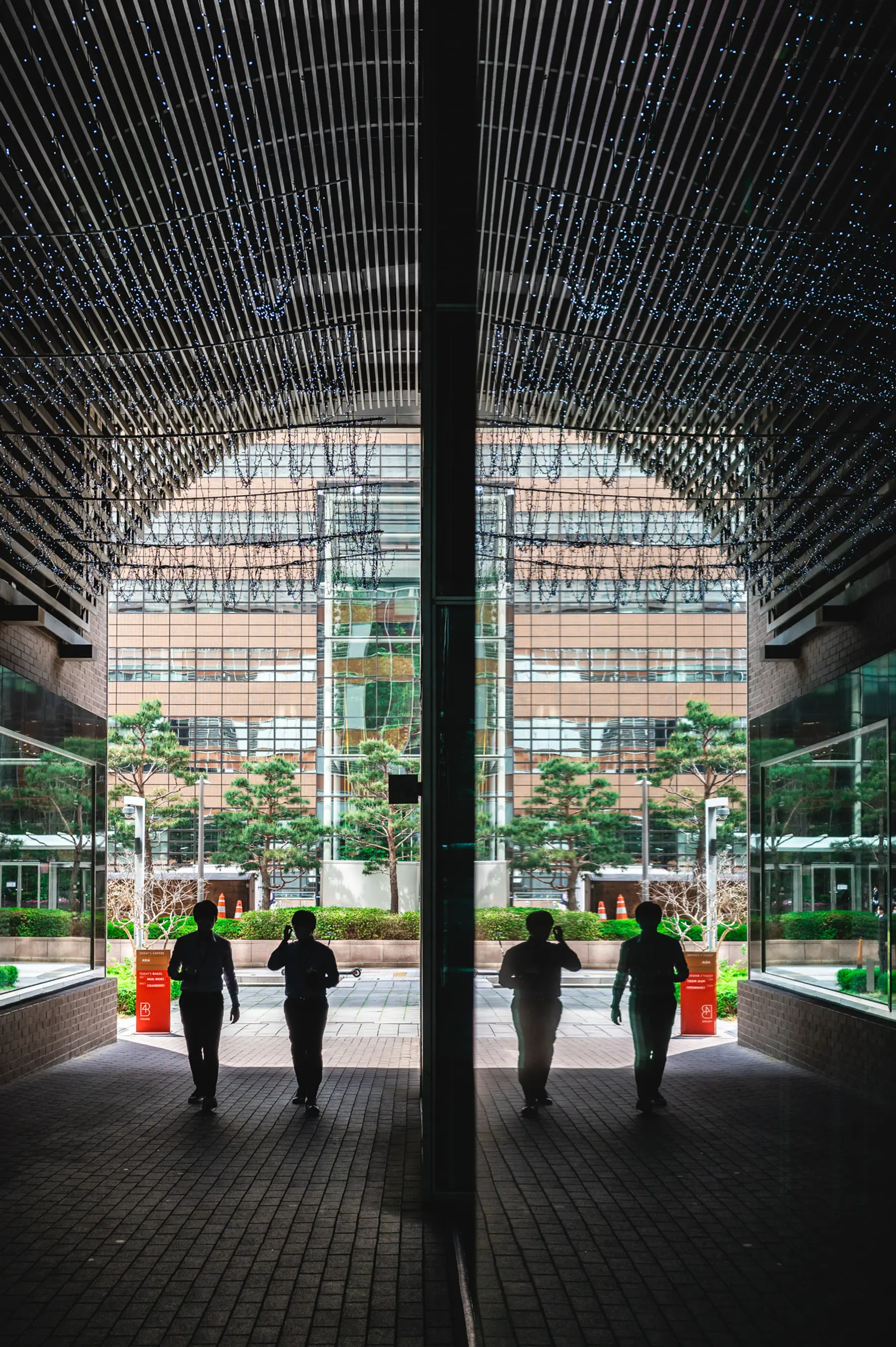 Two men walk in silhouette through a tunnel as their reflection appears in the opposite wall in Jonggak, Seoul