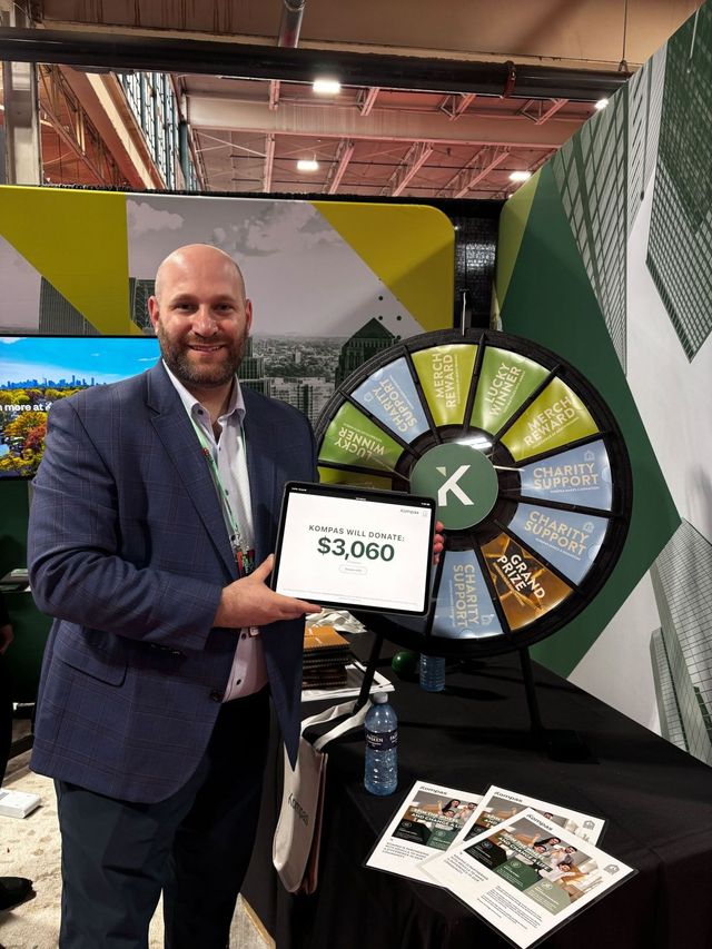 A Kompas team member at a trade-show booth with a prize wheel