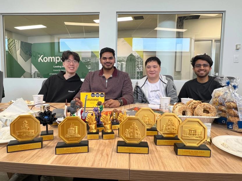 Kompas team members at a table lined with gold sprint award trophies