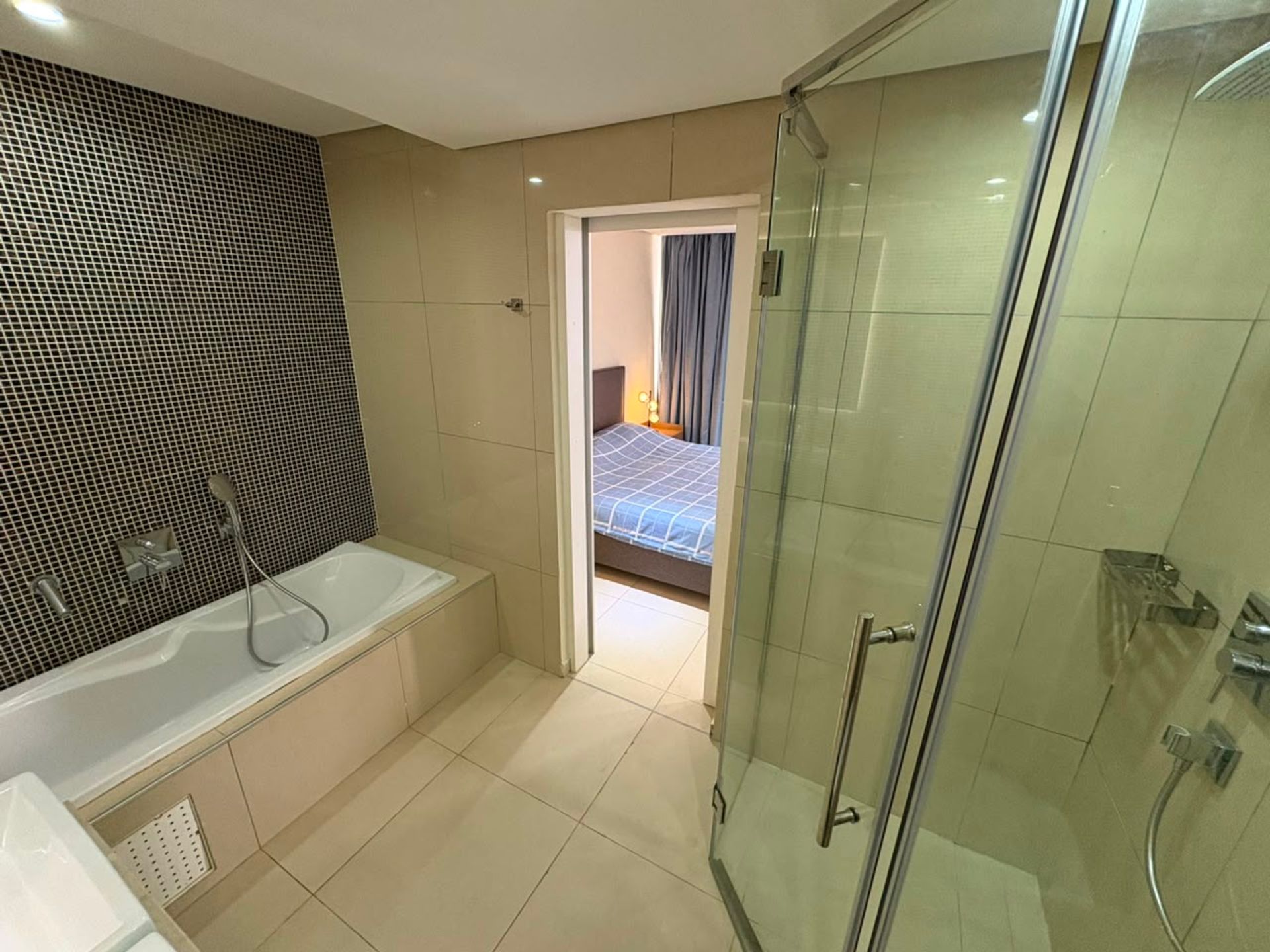 Salle de bain avec baignoire, mosaïque foncée et douche vitrée, vue sur la chambre, duplex à Mermoz