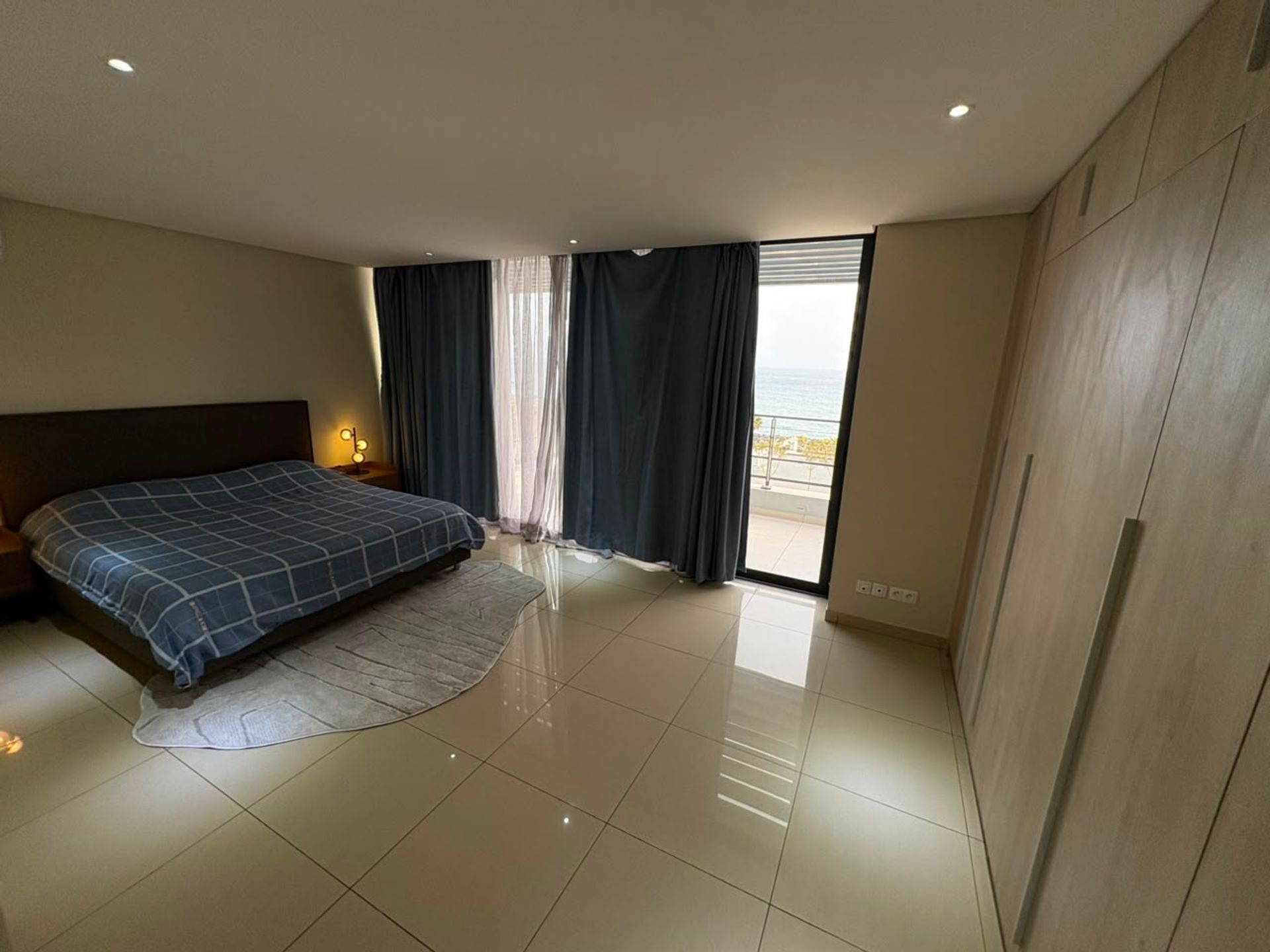 Chambre spacieuse d'un duplex à Mermoz avec lit double, sol carrelé brillant et baie vitrée vue mer