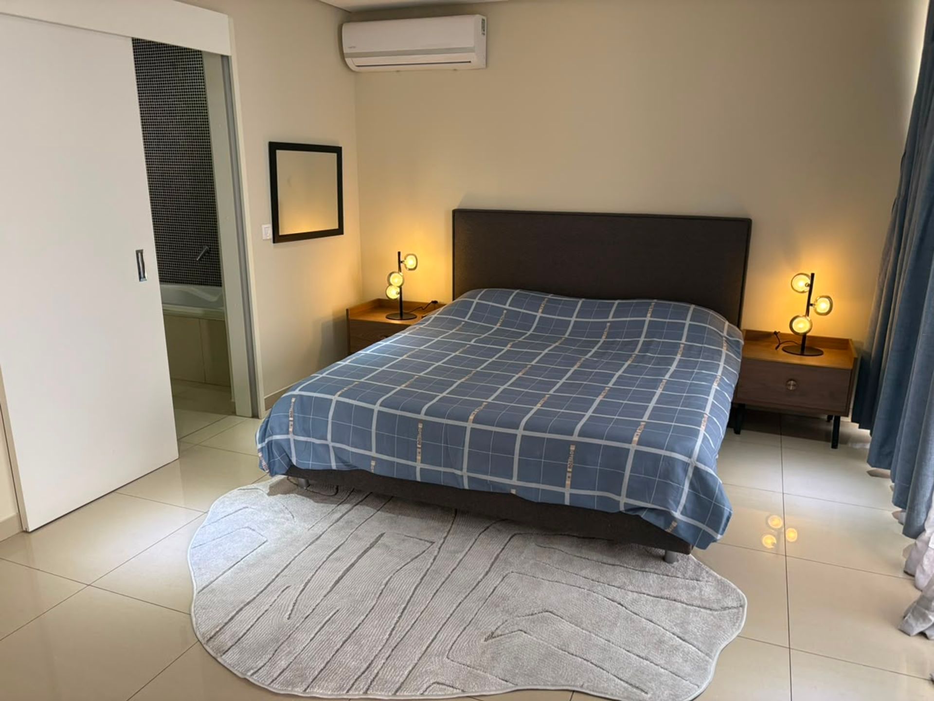 Chambre lumineuse d un duplex meuble a Mermoz, lit a couette a carreaux bleus, tapis gris et climatiseur mural