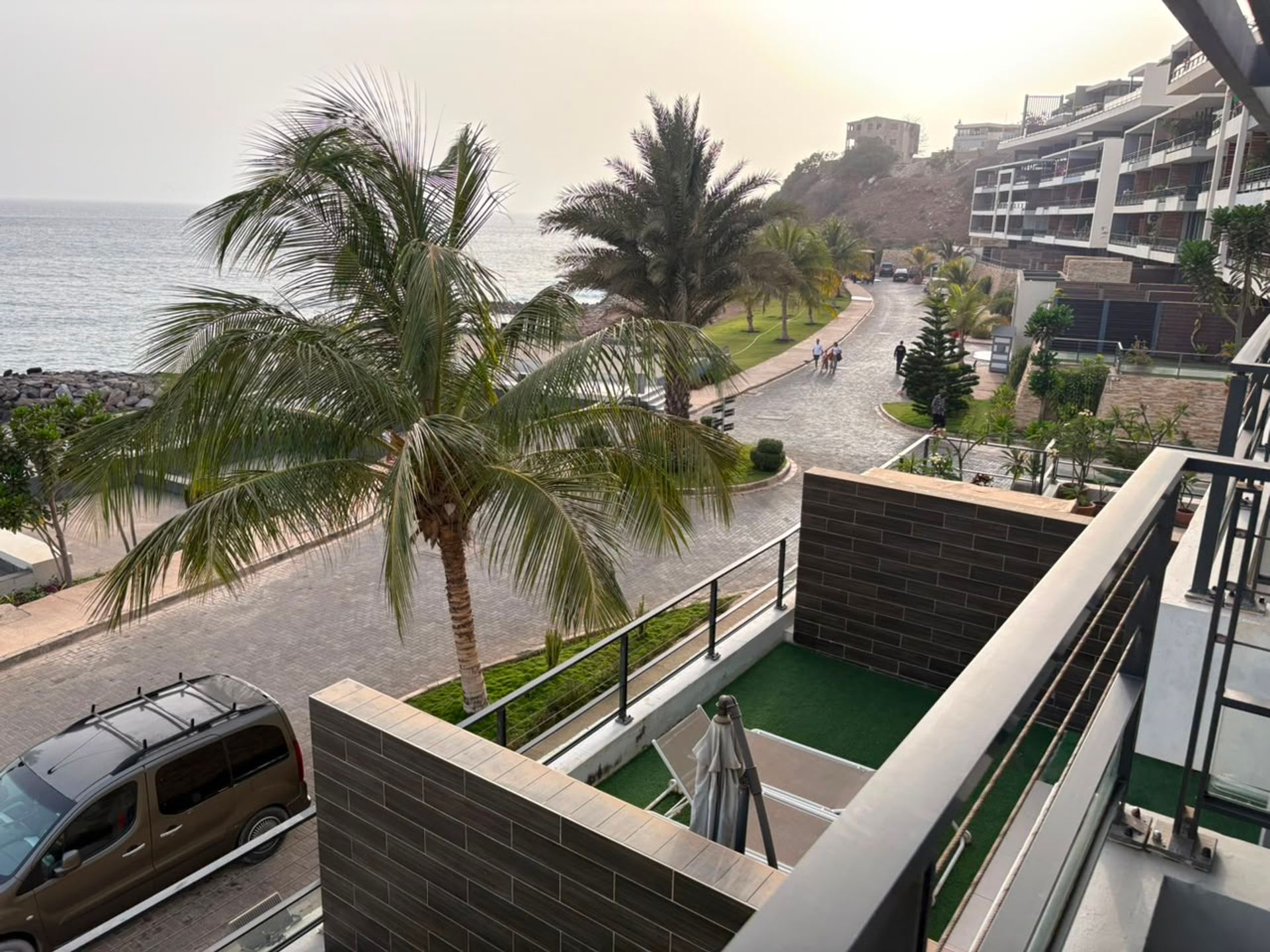 Vue depuis un balcon d'un duplex à Mermoz sur un palmier, une allée pavée bordée de résidences et l'océan