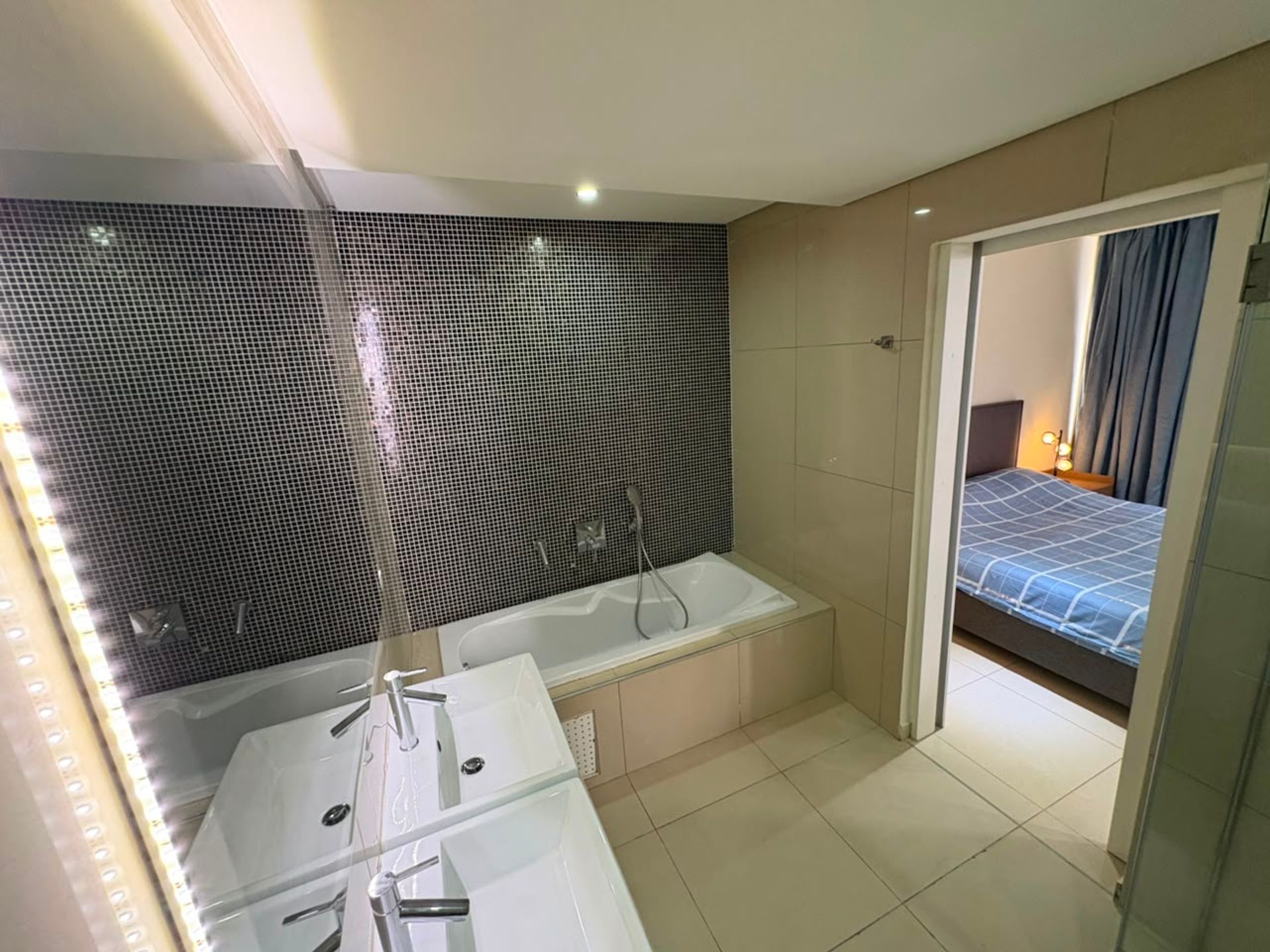Salle de bain d'un duplex meublé à Mermoz avec baignoire, mosaïque noire et vue sur la chambre attenante