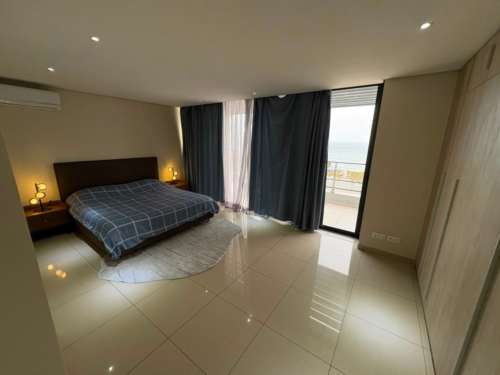 Chambre haut standing avec lit à carreaux bleus, baie vitrée et vue mer, duplex à Mermoz