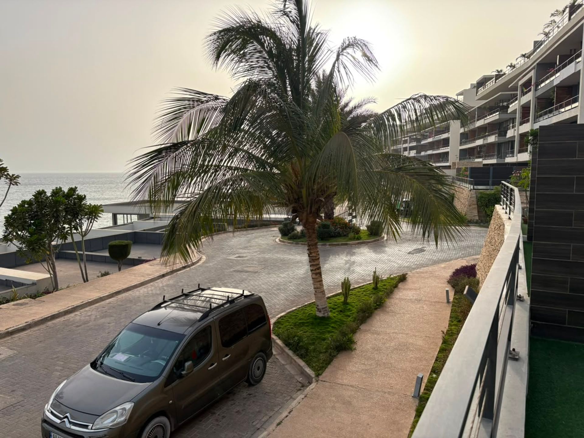 Vue en hauteur depuis un duplex à Mermoz sur une allée pavée, palmier et bâtiments résidentiels face à l'océan