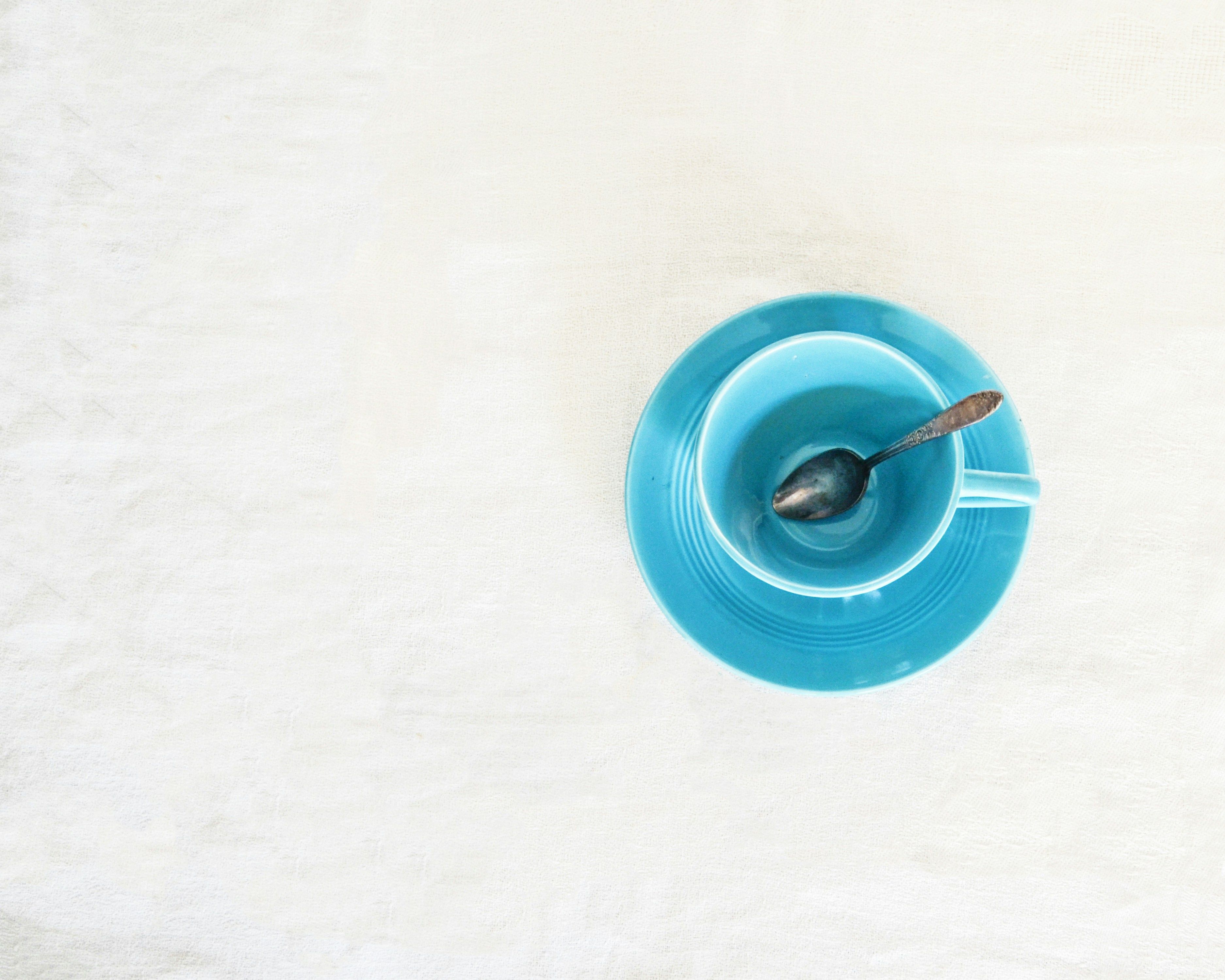 Photo of a blue tea cup containing a teaspoon, seen from above on a white background, by Debby Hudson on Unsplash