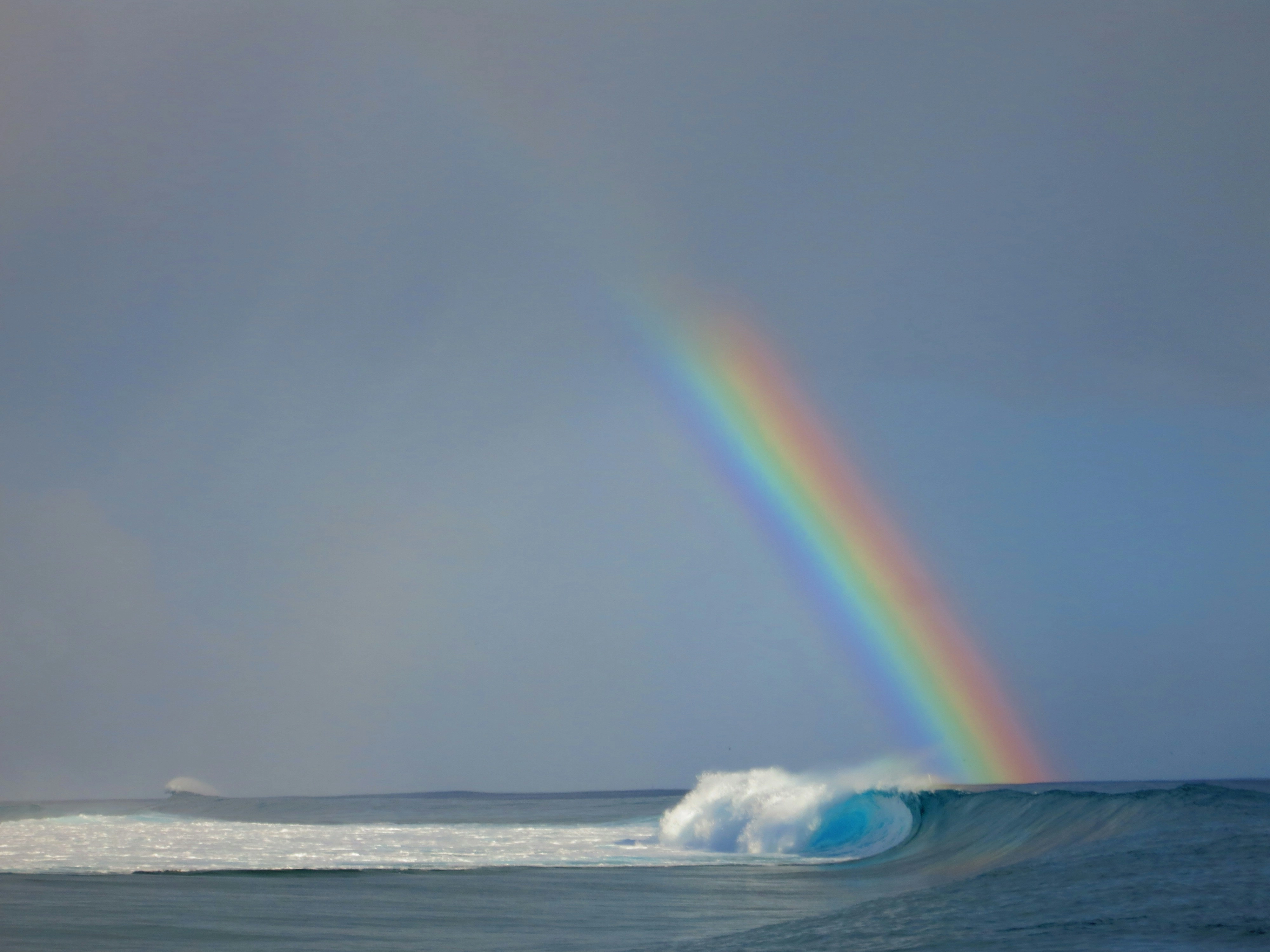 a photo of a rainbow in a stormy sky over a breaking wave by Lucie Dawson via Unsplash
