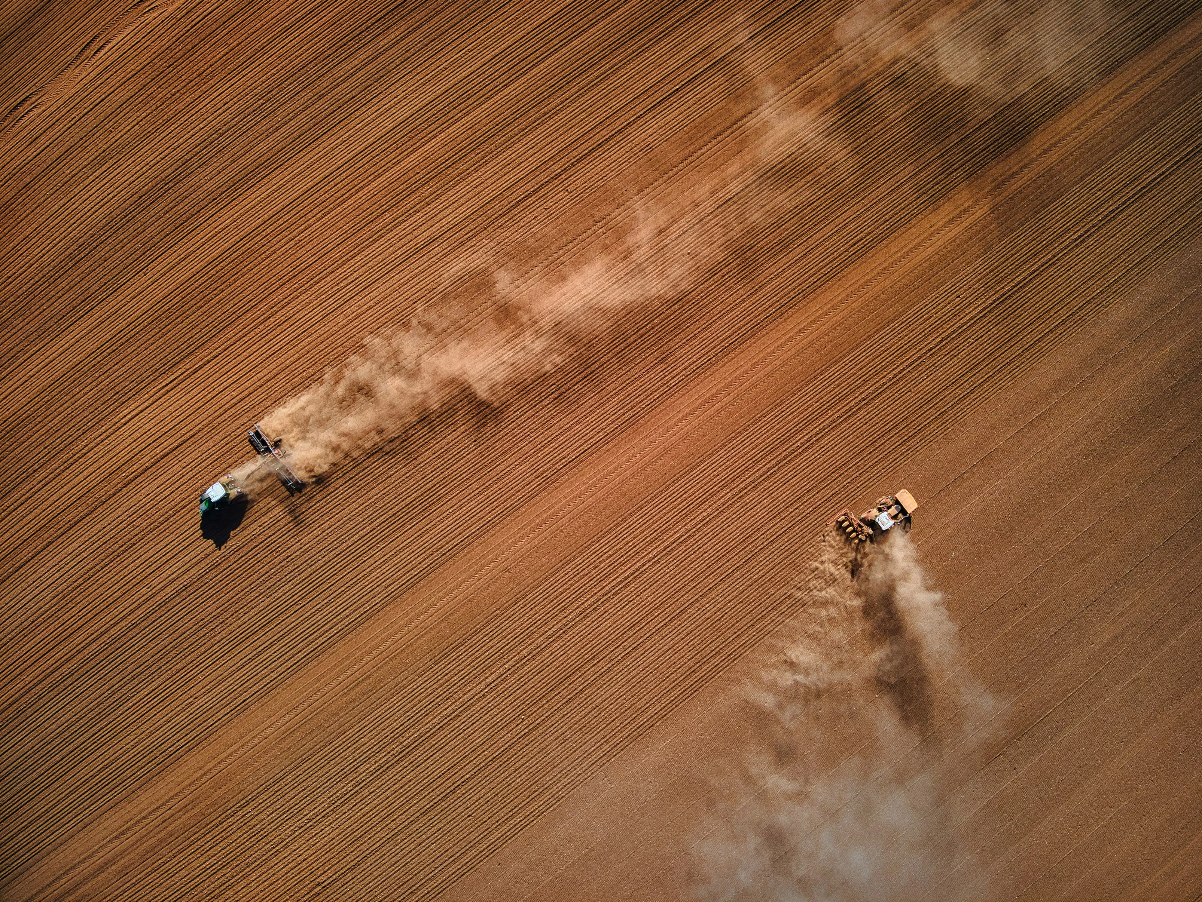 Aerial photo of farm machinery working in a ploughed field of brown soil by Red Zeppelin Unsplash