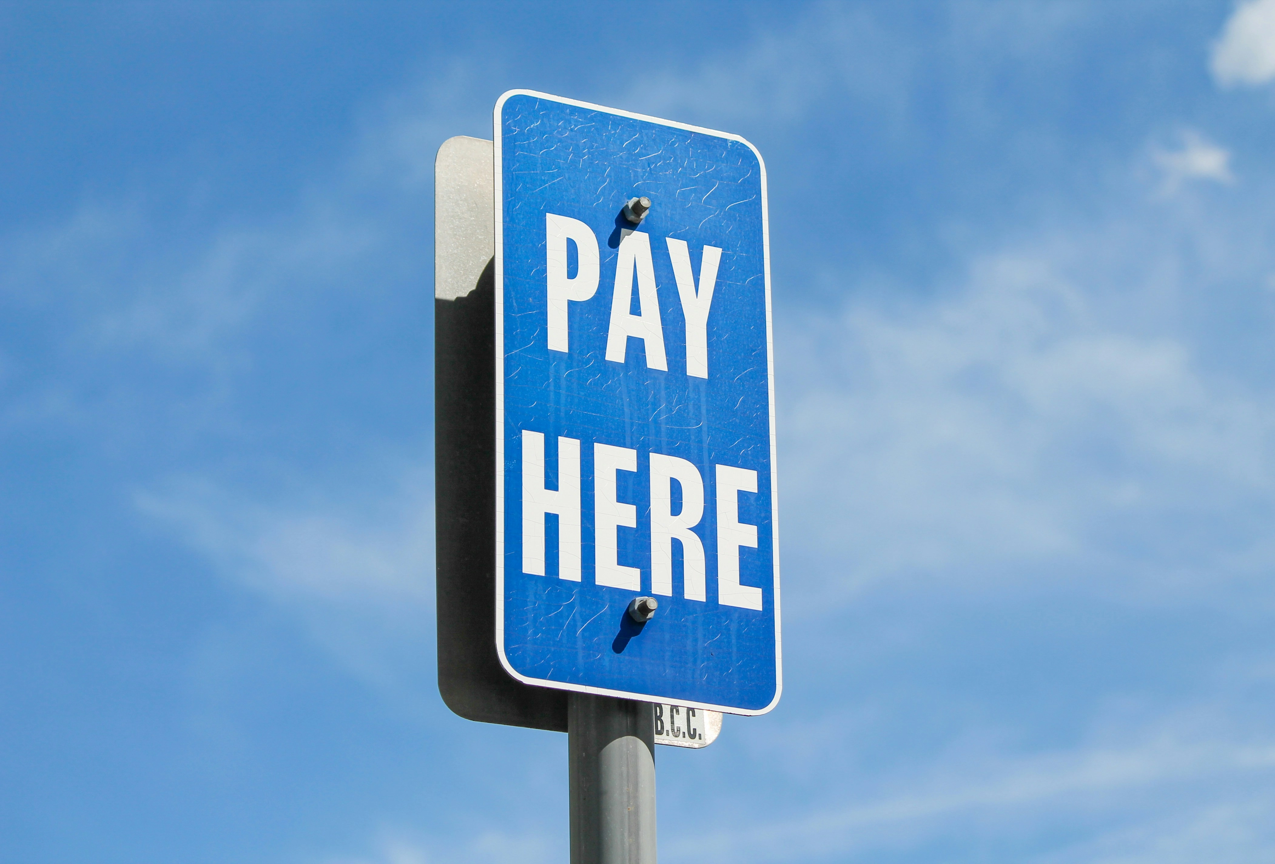 A blue sign that says "PAY HERE" against a blue sky with some light cloud