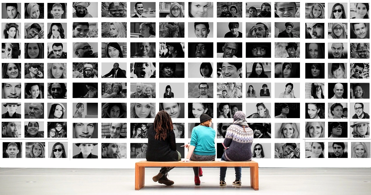 a photo of three friends sitting on a bench, viewing a wall of black-and-white portraits