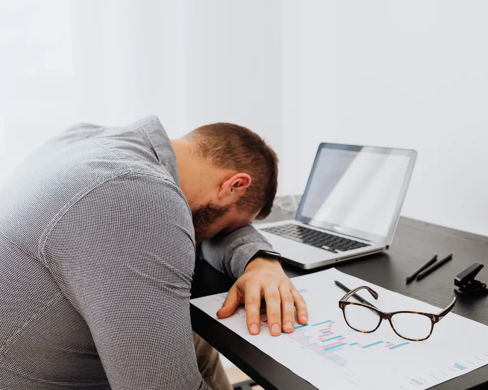 Man with his head on the desk in front of laptop