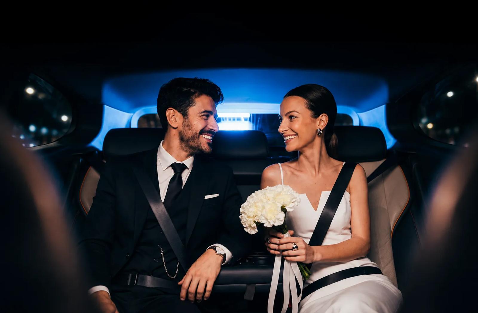 Bride and groom in the back seat of a Rhino car at night, on their way to the celebration