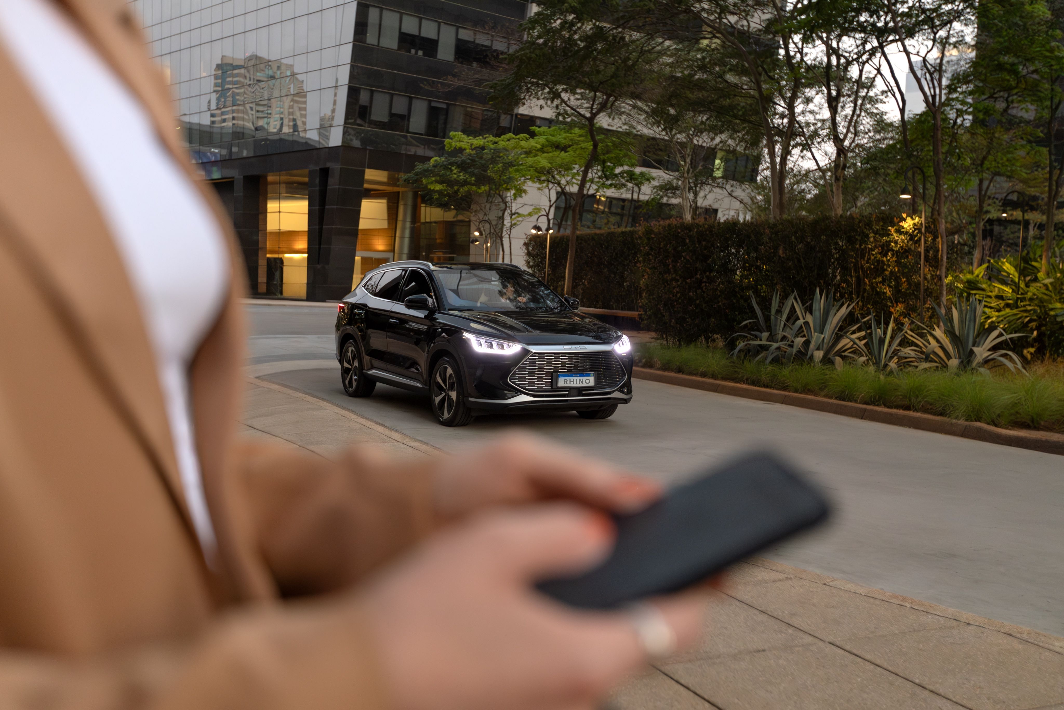 Passageiro com celular aguarda SUV blindado preto da Rhino em São Paulo