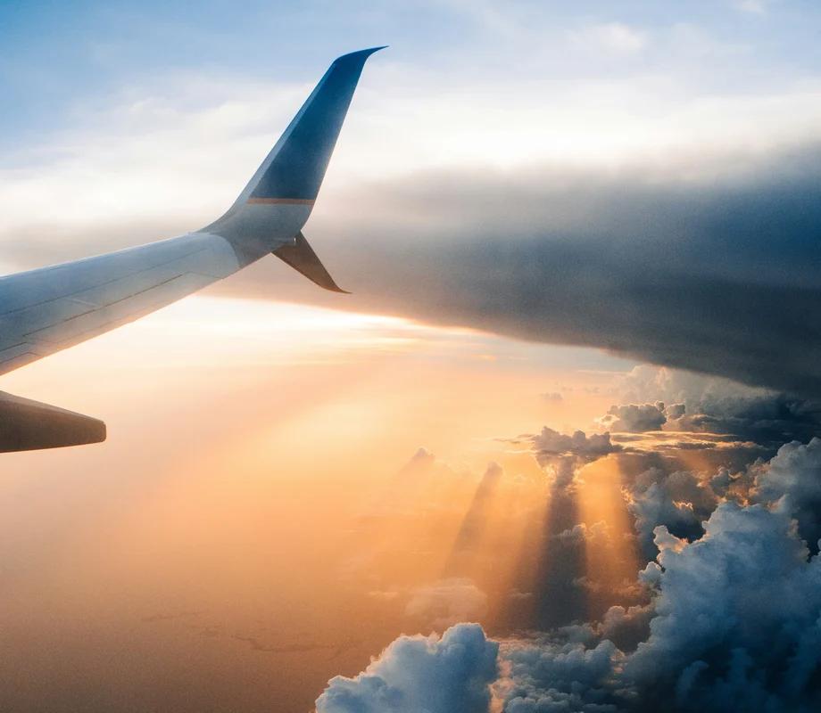 A asa de um avião acima de nuvens iluminadas pelo sol