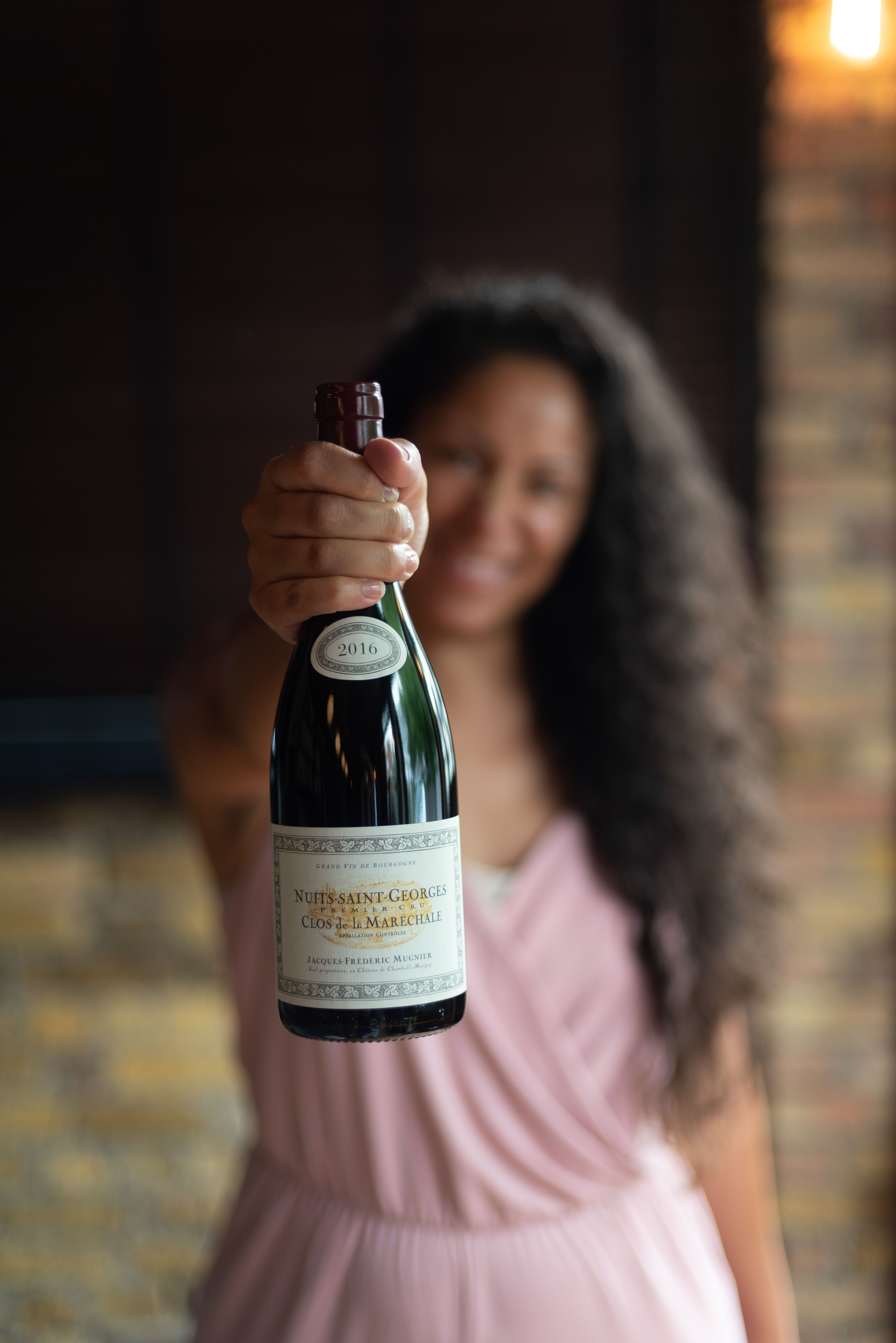 Woman holding bottle of Nuits-Saint-Georges Burgundy toward camera, representing how wine choices reveal personal identity, taste preferences, and social signals