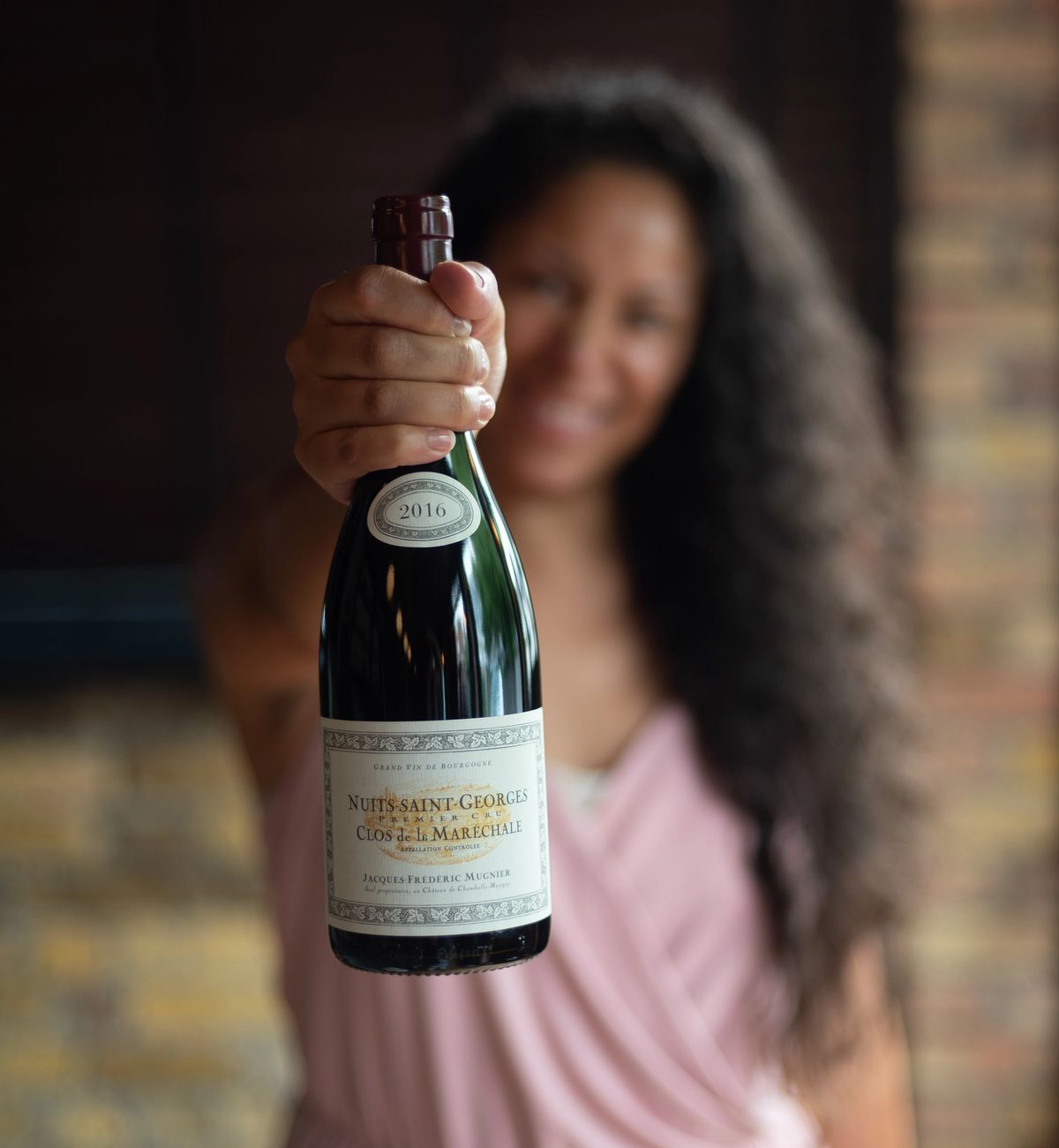 Woman holding bottle of Nuits-Saint-Georges Burgundy toward camera, representing how wine choices reveal personal identity, taste preferences, and social signals