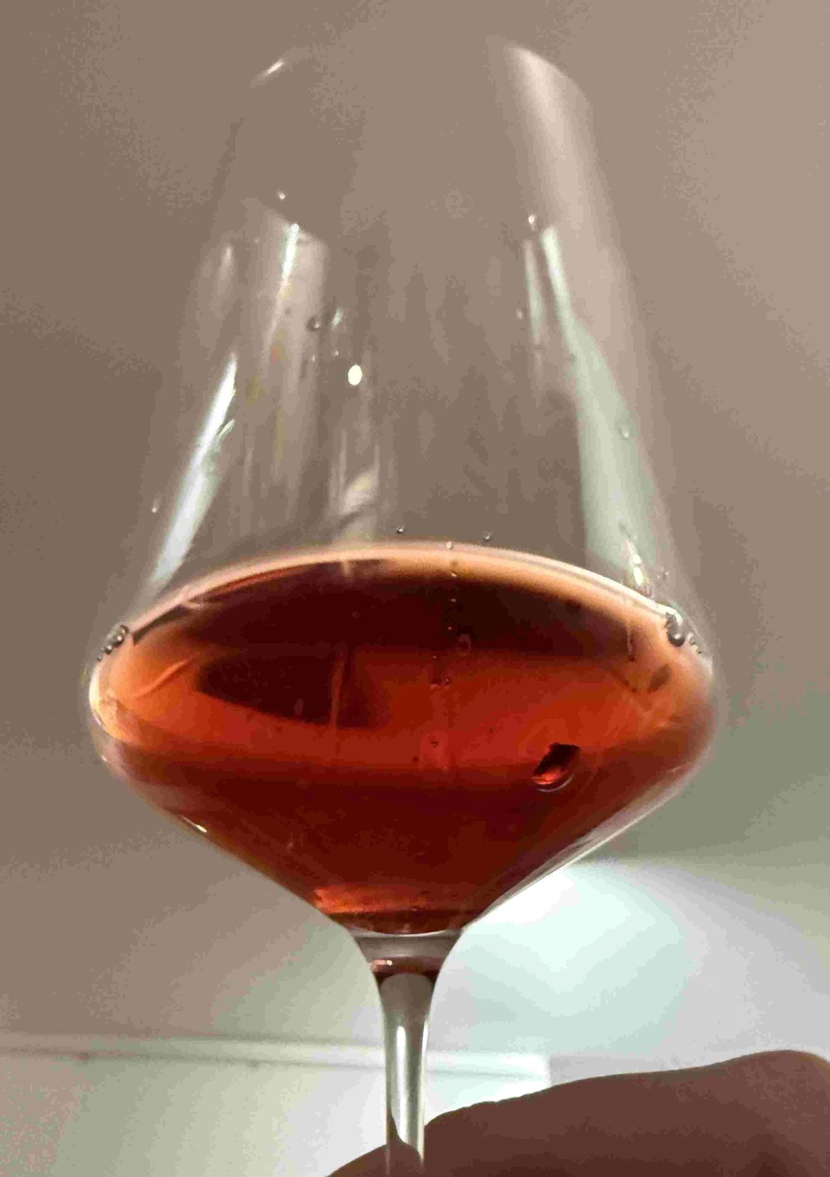 A close-up of a wine glass held at an angle against natural light, showing colour and clarity. Alt text: A glass of wine held against natural light, showing depth of colour and clarity.