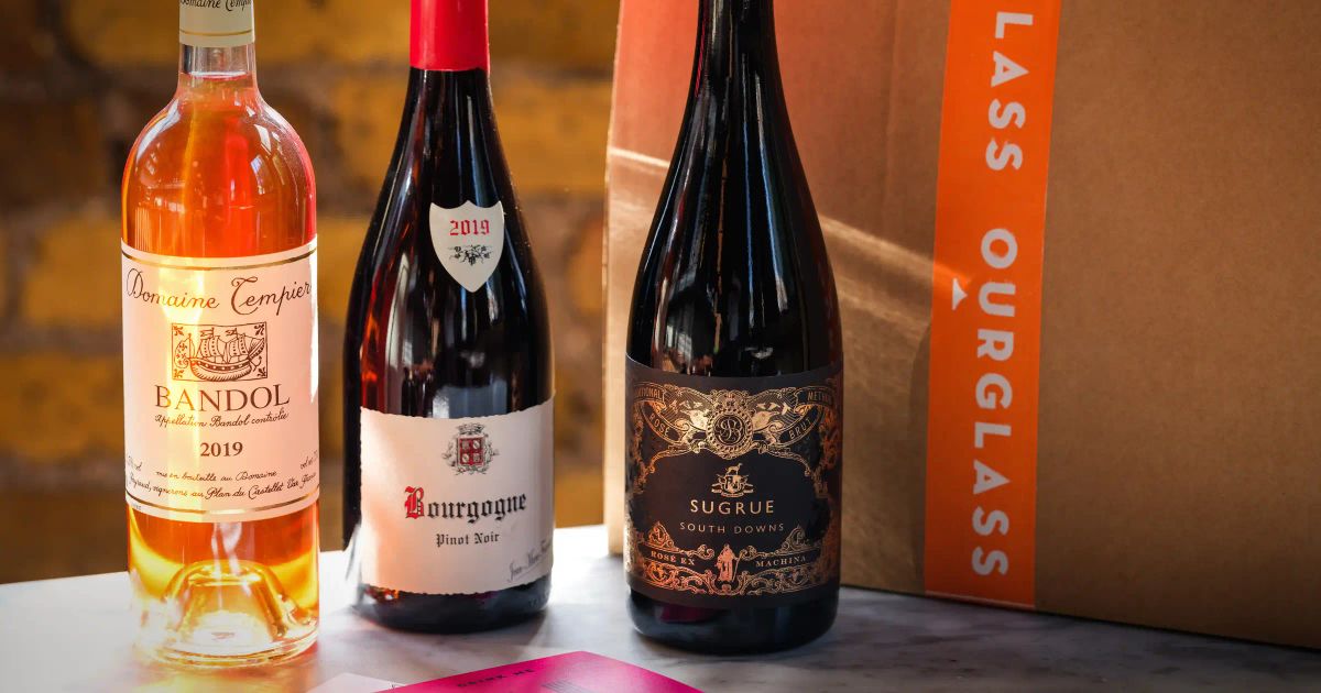 Three wine bottles from an Ourglass subscription box: Domaine Tempier Bandol rosé, Fourrier Bourgogne Pinot Noir, and Sugrue South Downs sparkling, with postcards