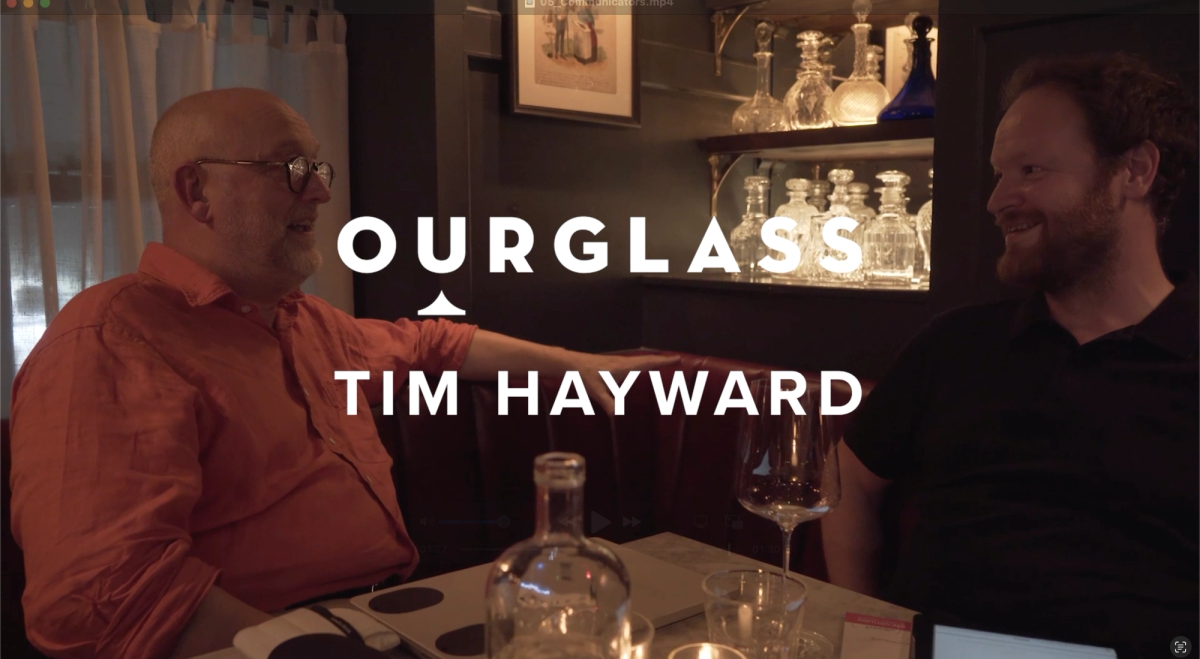Tim Hayward and Benedict Johnson chat over wine in a dimly lit corner of Noble Rot, surrounded by glassware, during the filming of the Ourglass Tapes video series.
