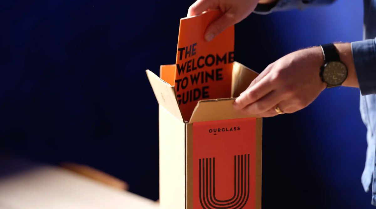 Ourglass wine subscription club box being opened, with The Welcome to Wine Guide being lifted out