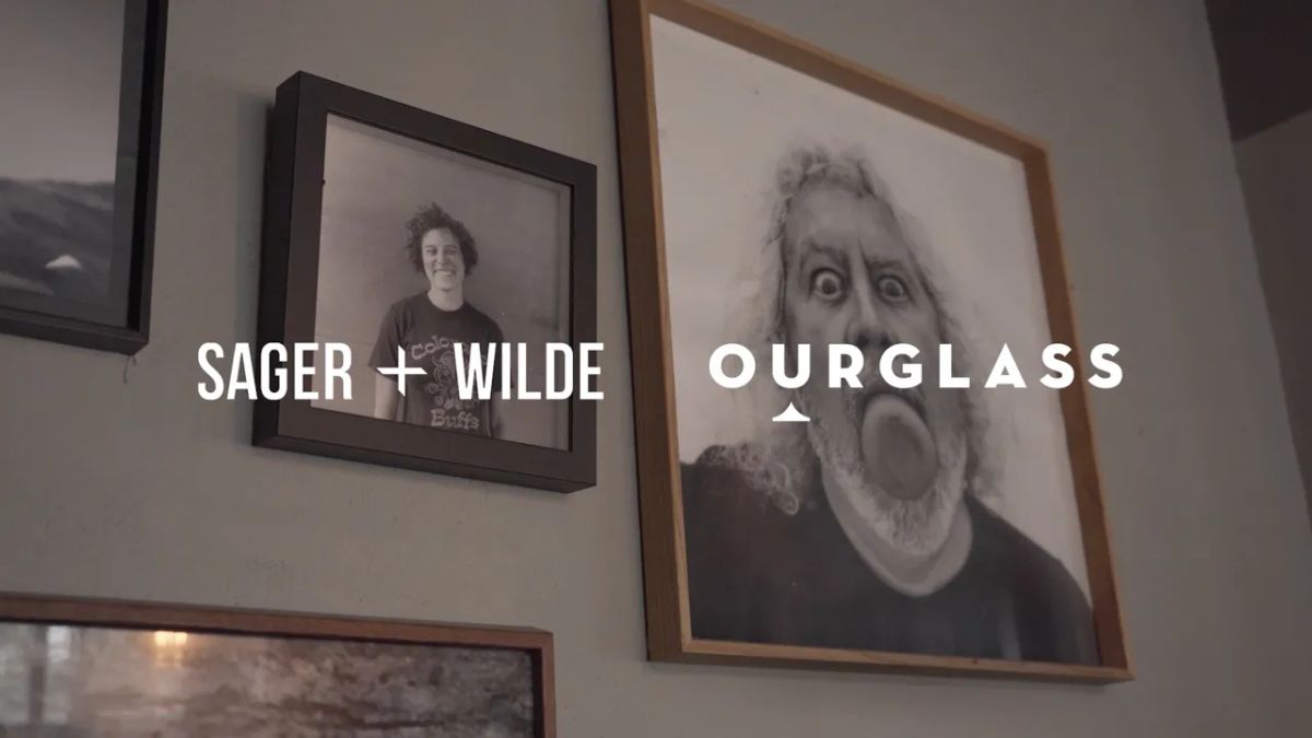 Framed photographs on the wall at Sager + Wilde, including a smiling young man and a surreal black-and-white portrait of Jim Clendenen, as featured in the Ourglass Tapes video series.