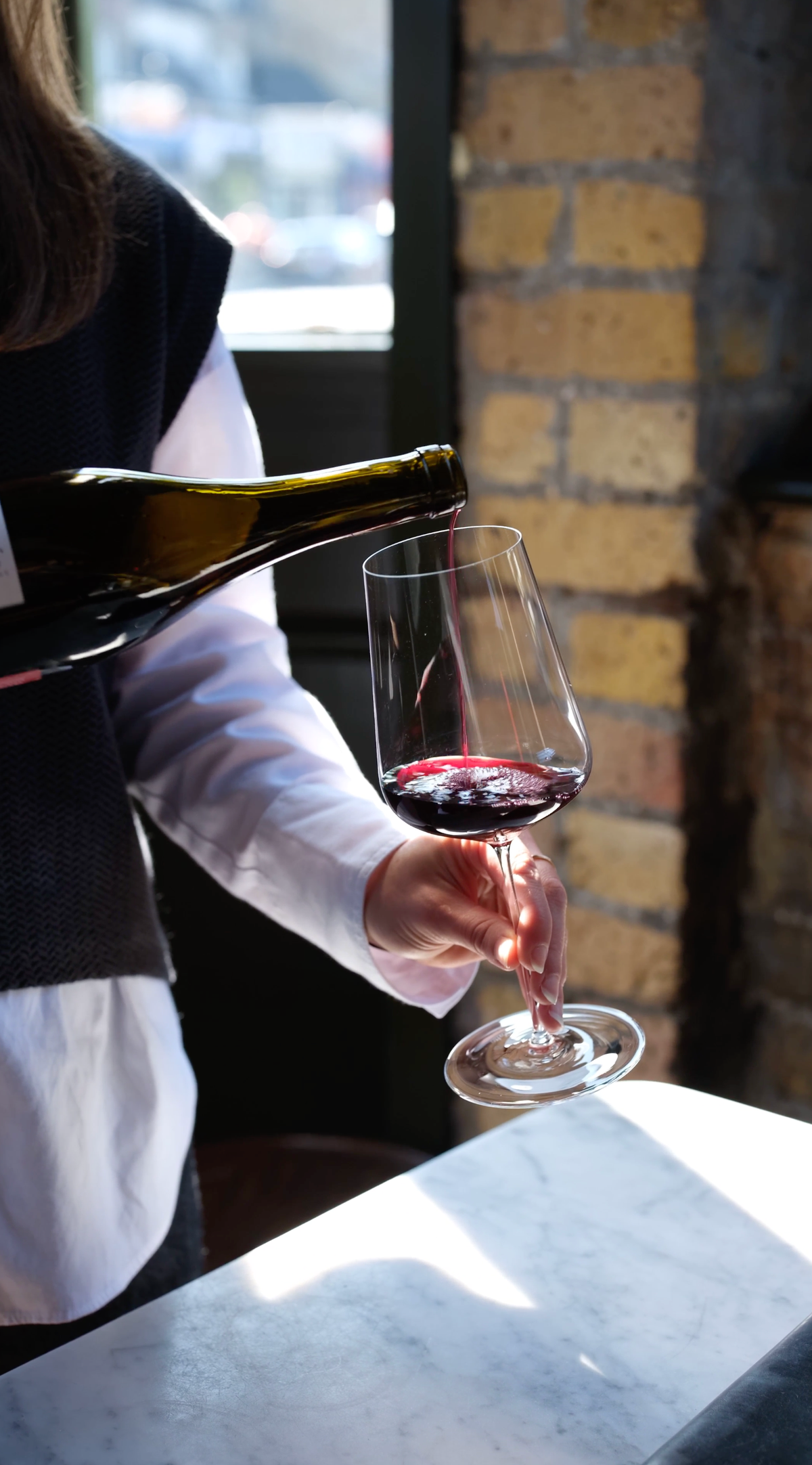 Pouring red wine into a glass on a marble table in natural light