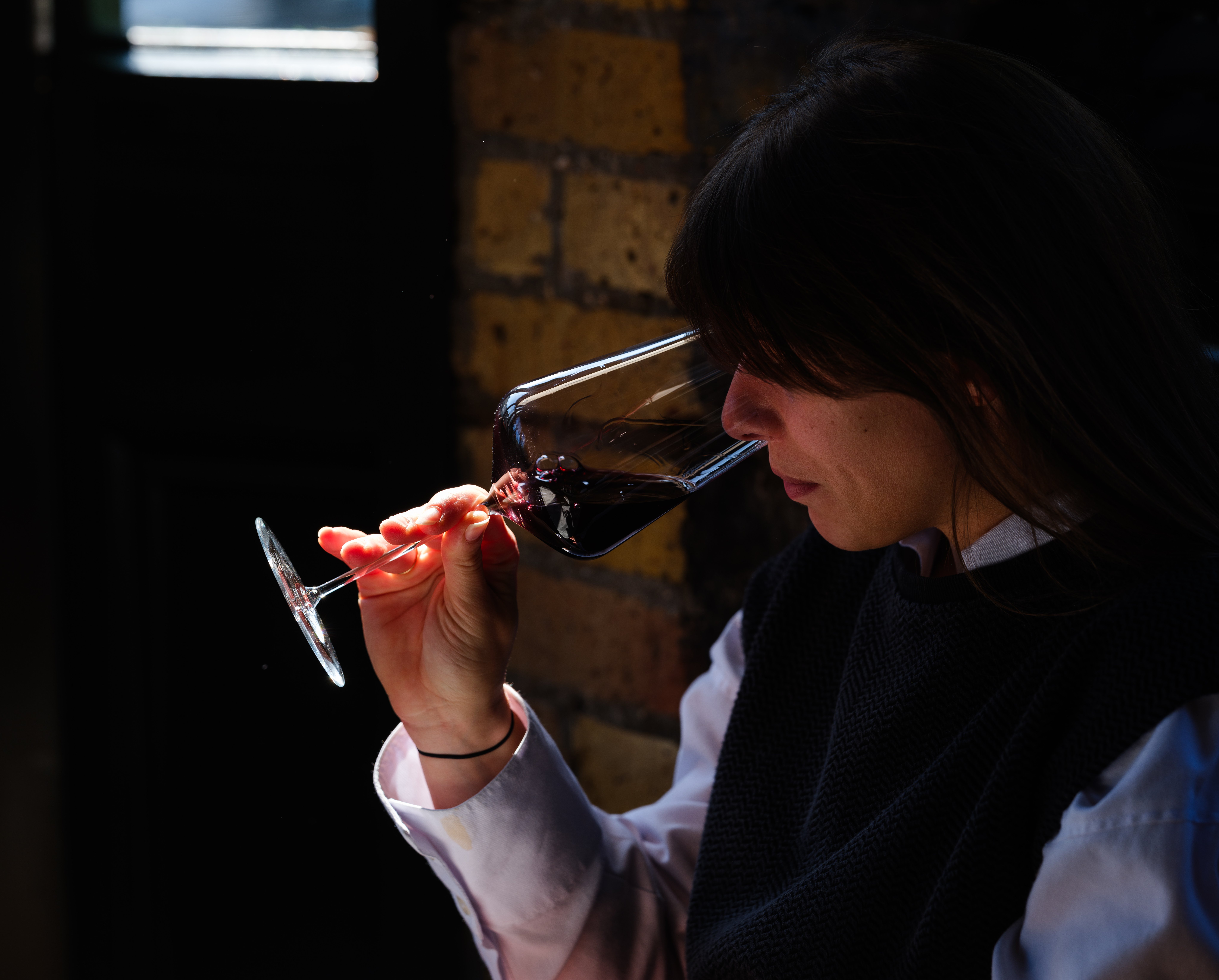 Woman smelling red wine in natural light at a marble table, capturing the sensory ritual of wine tasting in a modern restaurant setting.