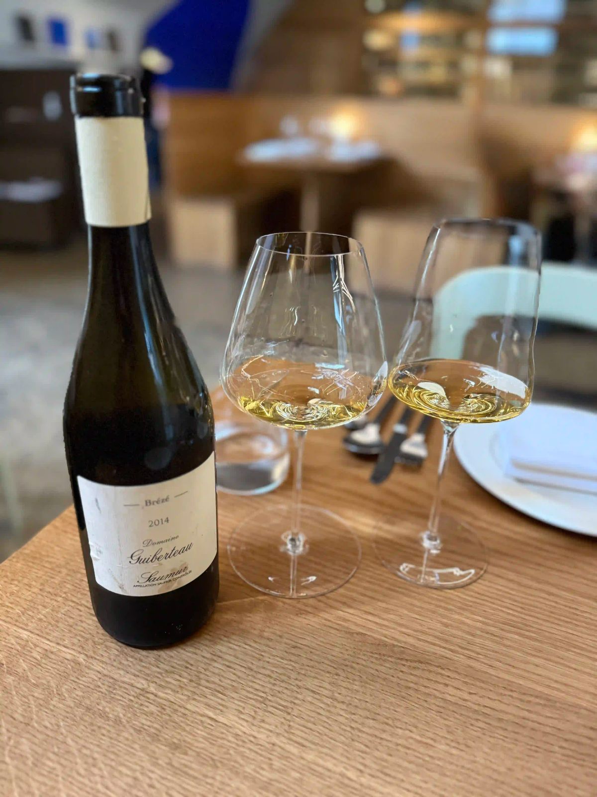 A single glass of white wine on a worn wooden table, natural afternoon light, no bottle in frame. Alt text: A glass of red wine on a wooden table in natural light.