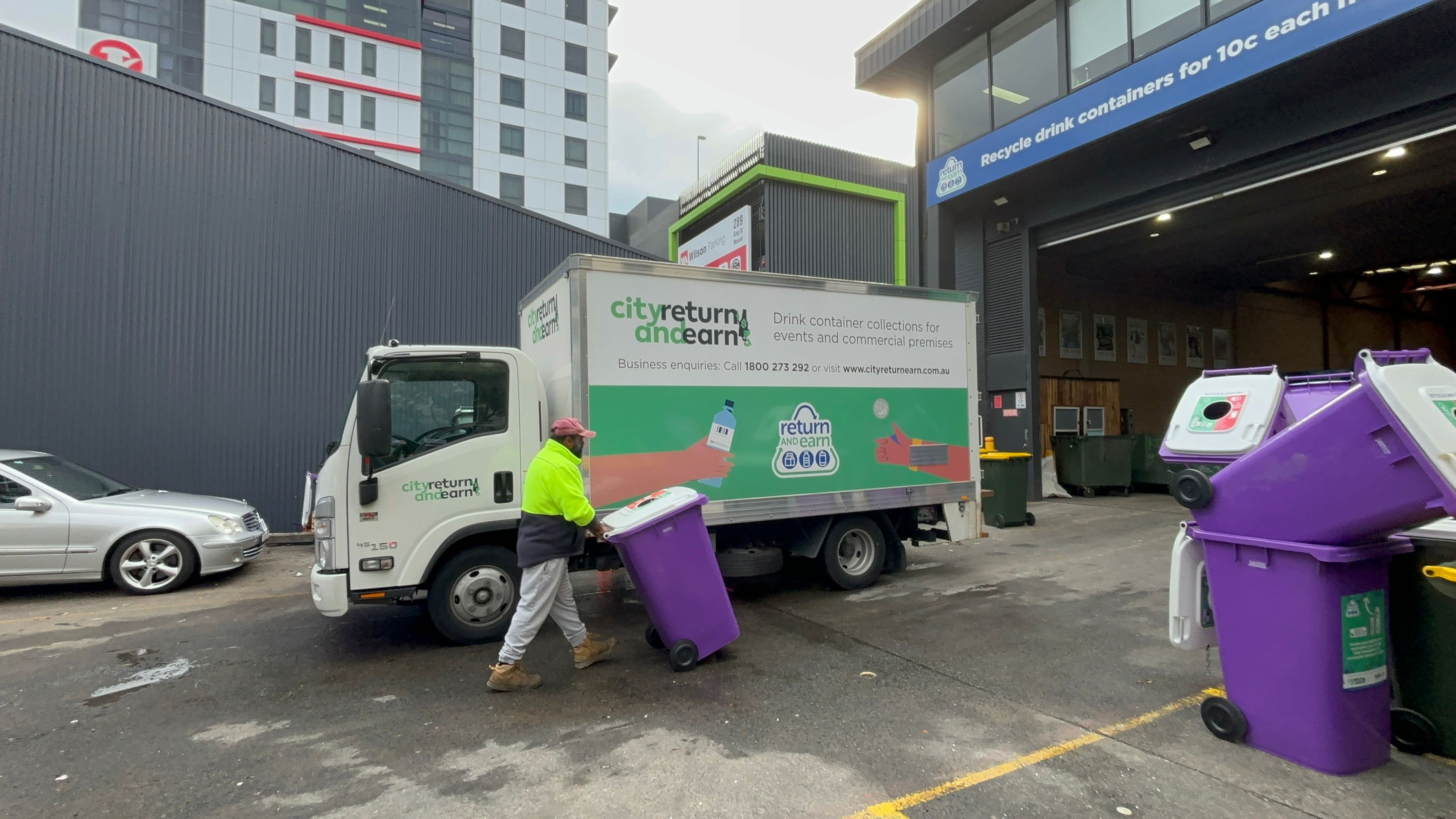 Staff wheeling a bin in front of the city return and earn truck 