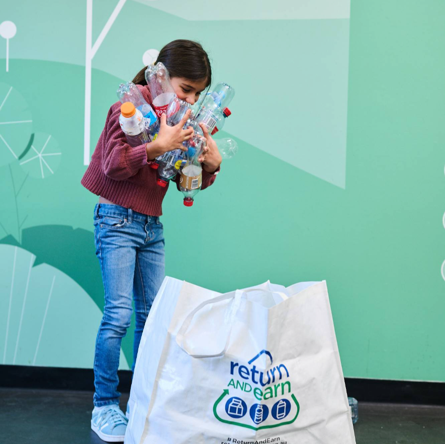 Child holding bottles over Return and Earn Bag