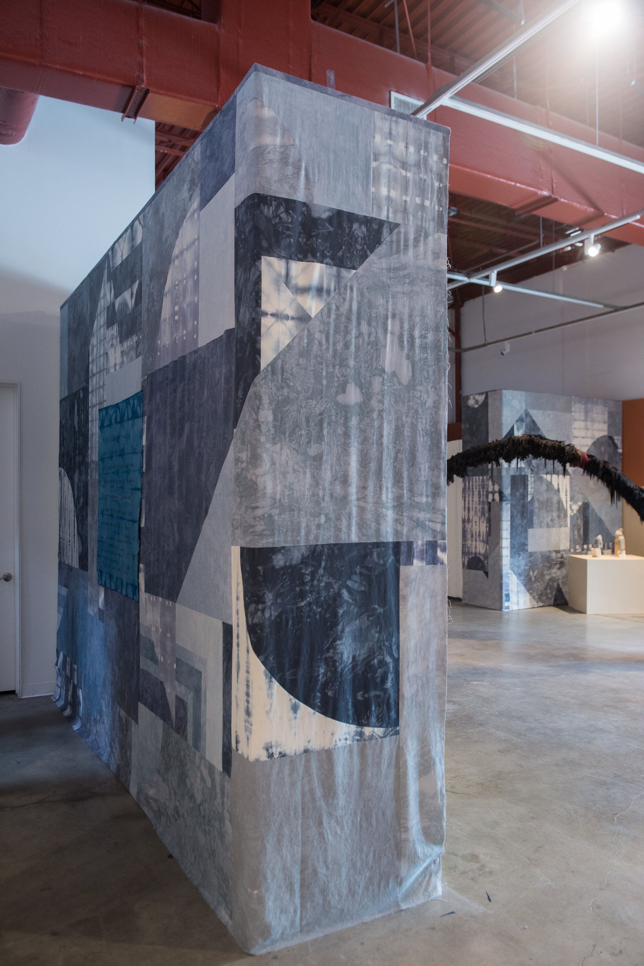 Large fabric-covered installation with abstract geometric patterns in gallery space